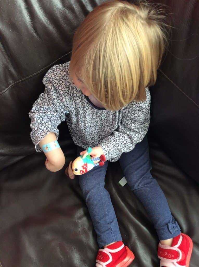 toddler holding tiny humpty dumpty toy and looking at a plaster on her wrist