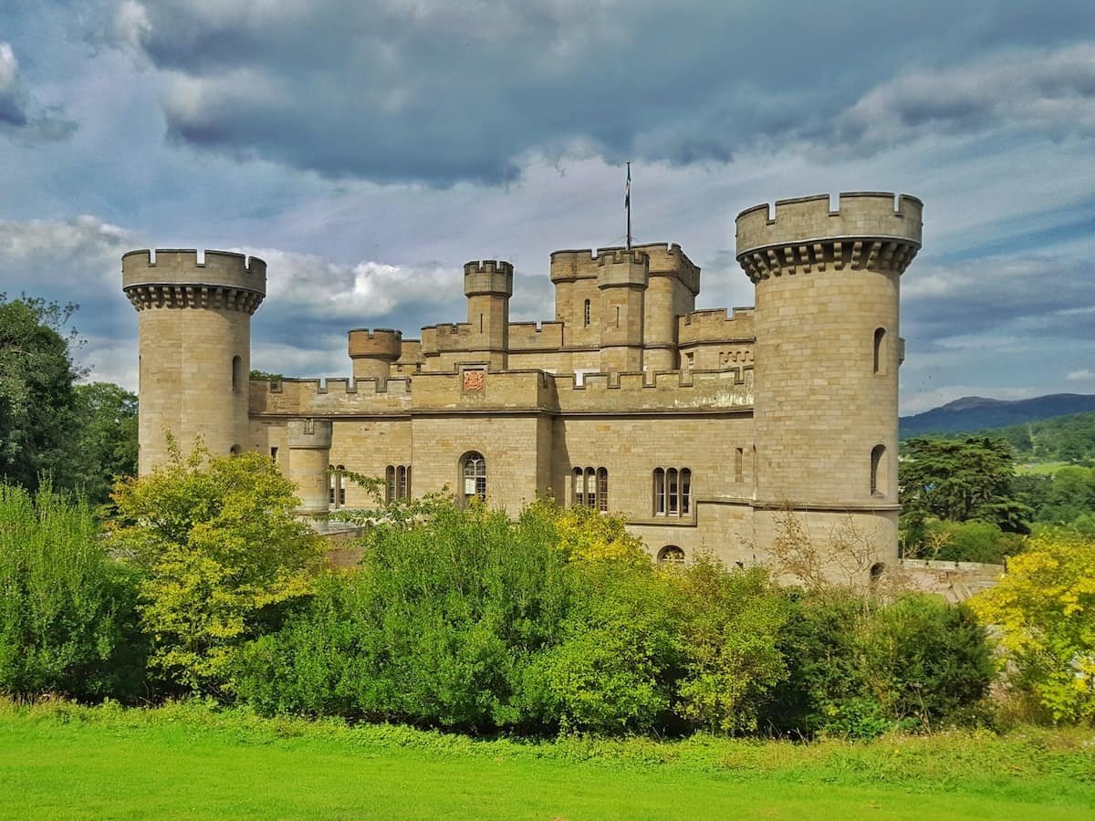 Eastnor Castle in Herefordshire with grass and bushes in front and cloudy sky above