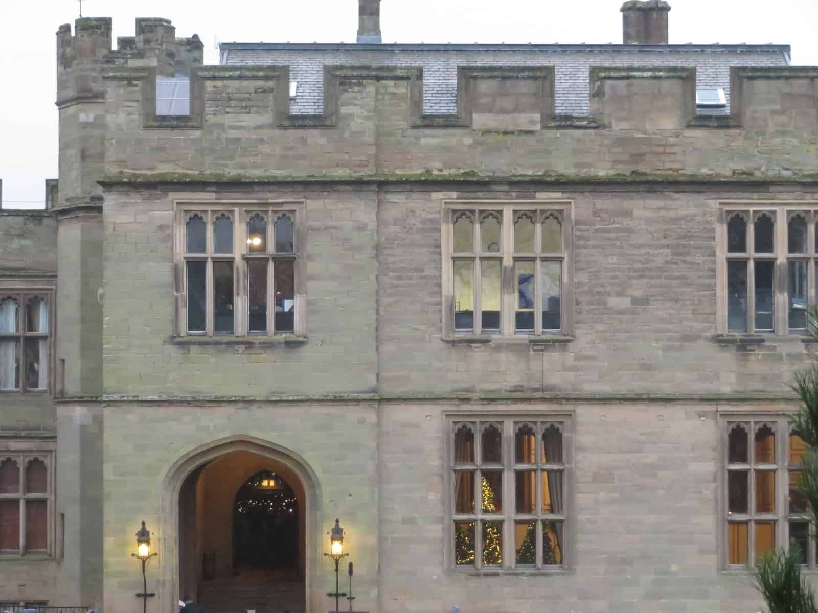 The exterior of the Great Hall at Warwick Castle. Through the window you can see a Christmas tree decorated with fairy lights. 