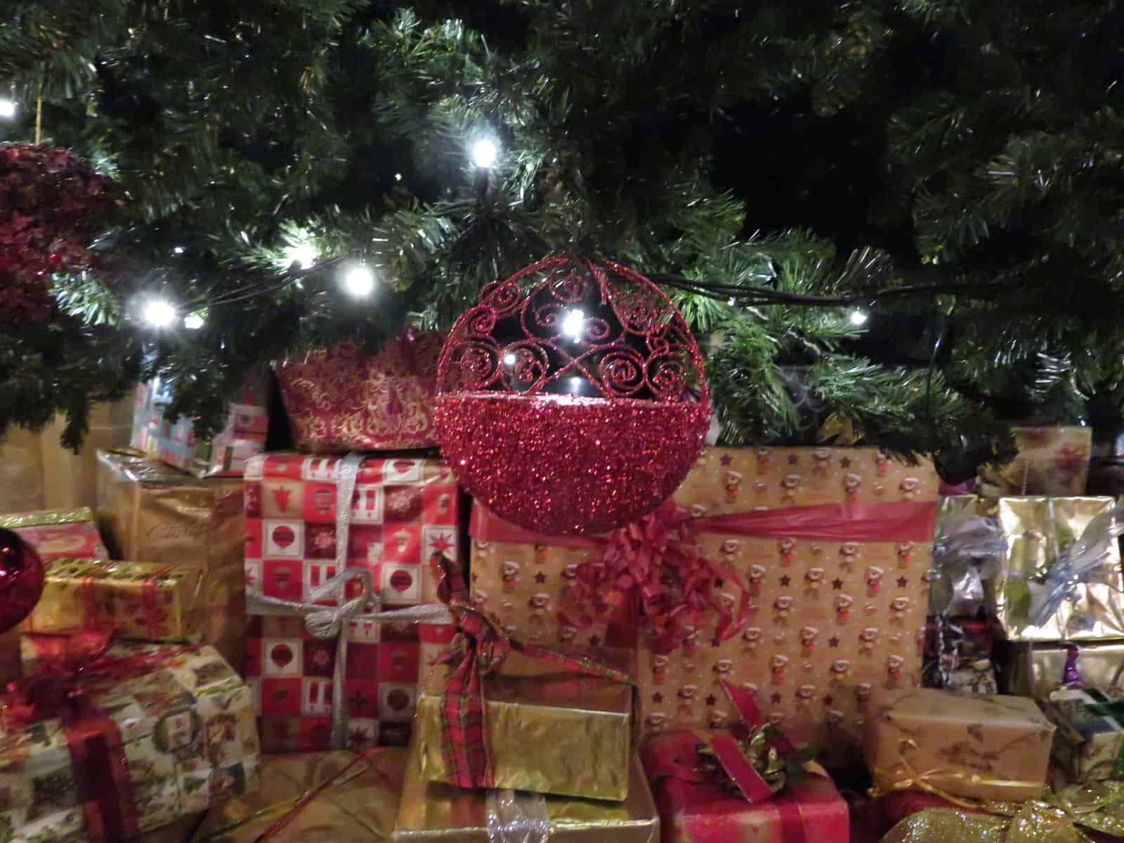 A Christmas decoration hangs from a tree with presents underneath and lights on the tree. 