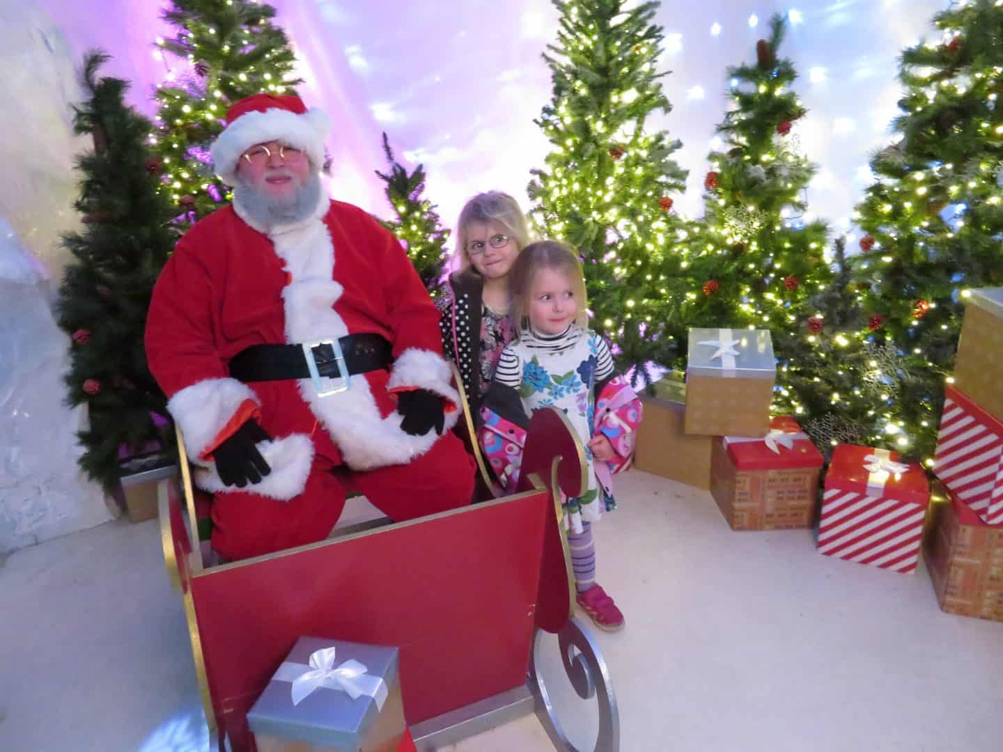 Santa in sleigh with two little girls, Christmas trees in the background