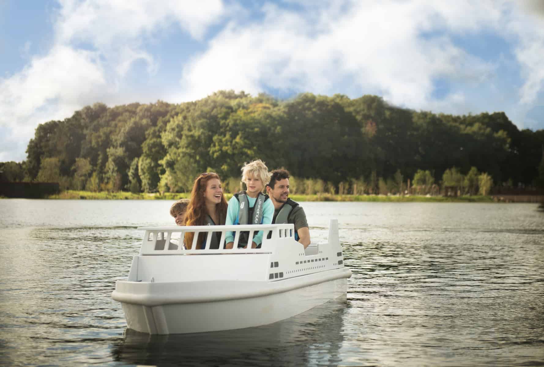 People riding in a small white boat on a lake with trees in the background