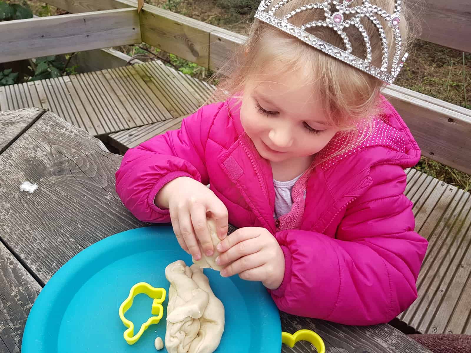 Little girl in pink coat and tiara creating a circuit from play dough with STEM science kit