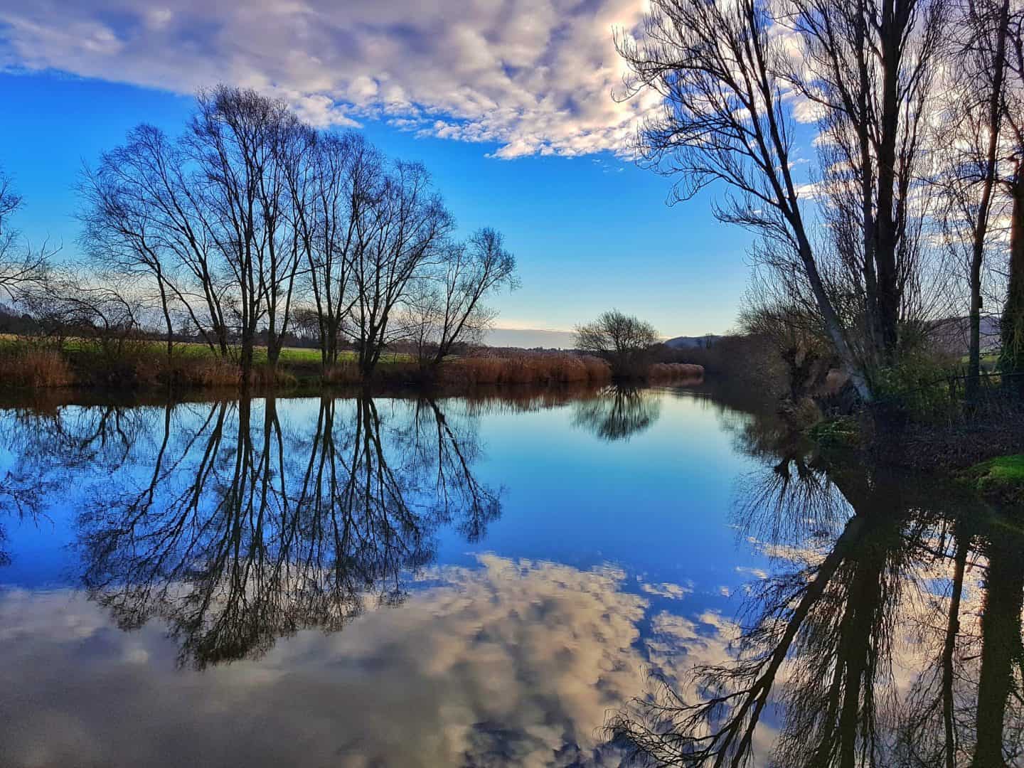 Wild swimming in Winter in a river with strong reflections of the clouds