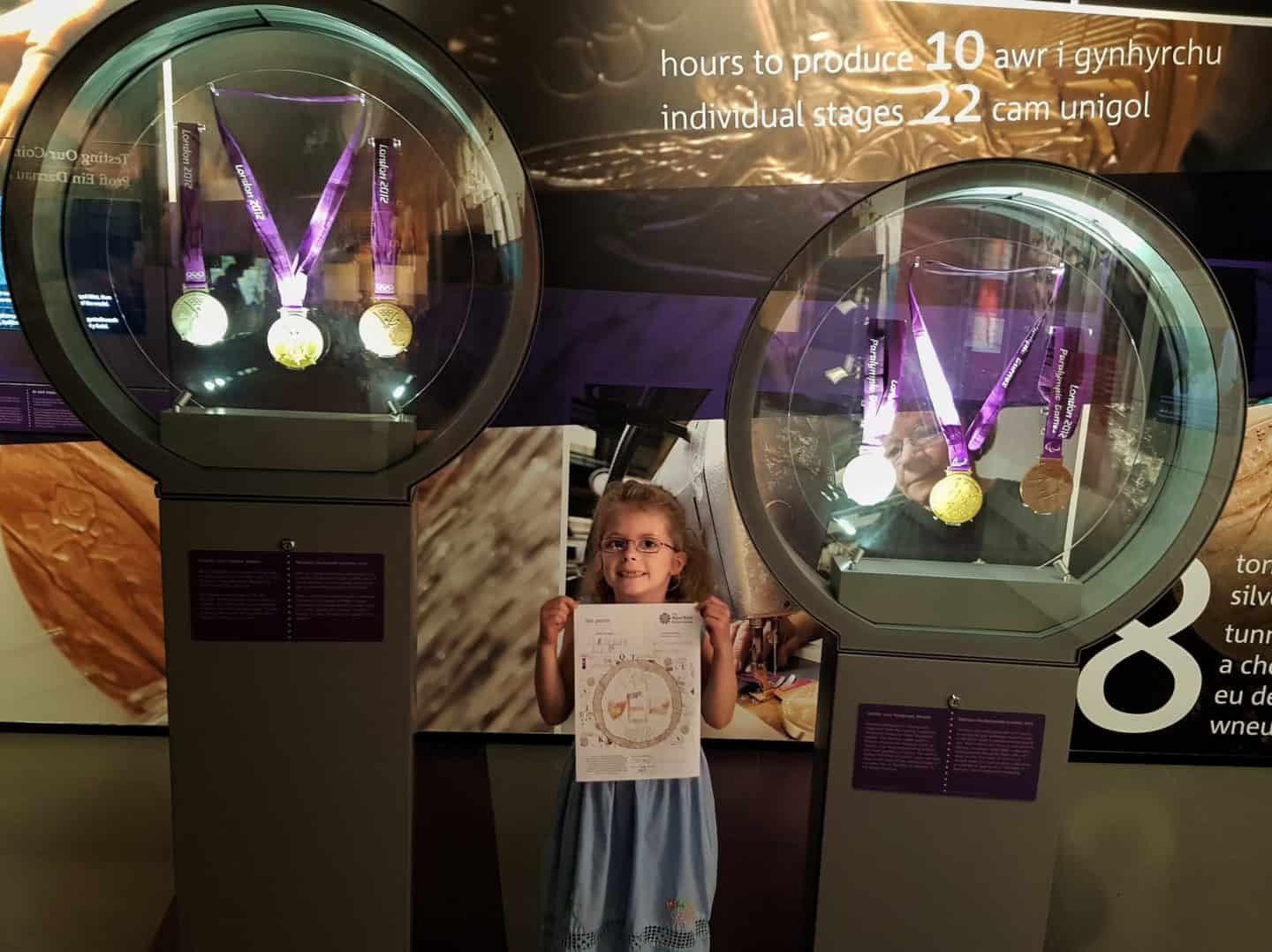 girl holding drawing next to Olympic and Paralympic medals on display at Royal Mint Experience