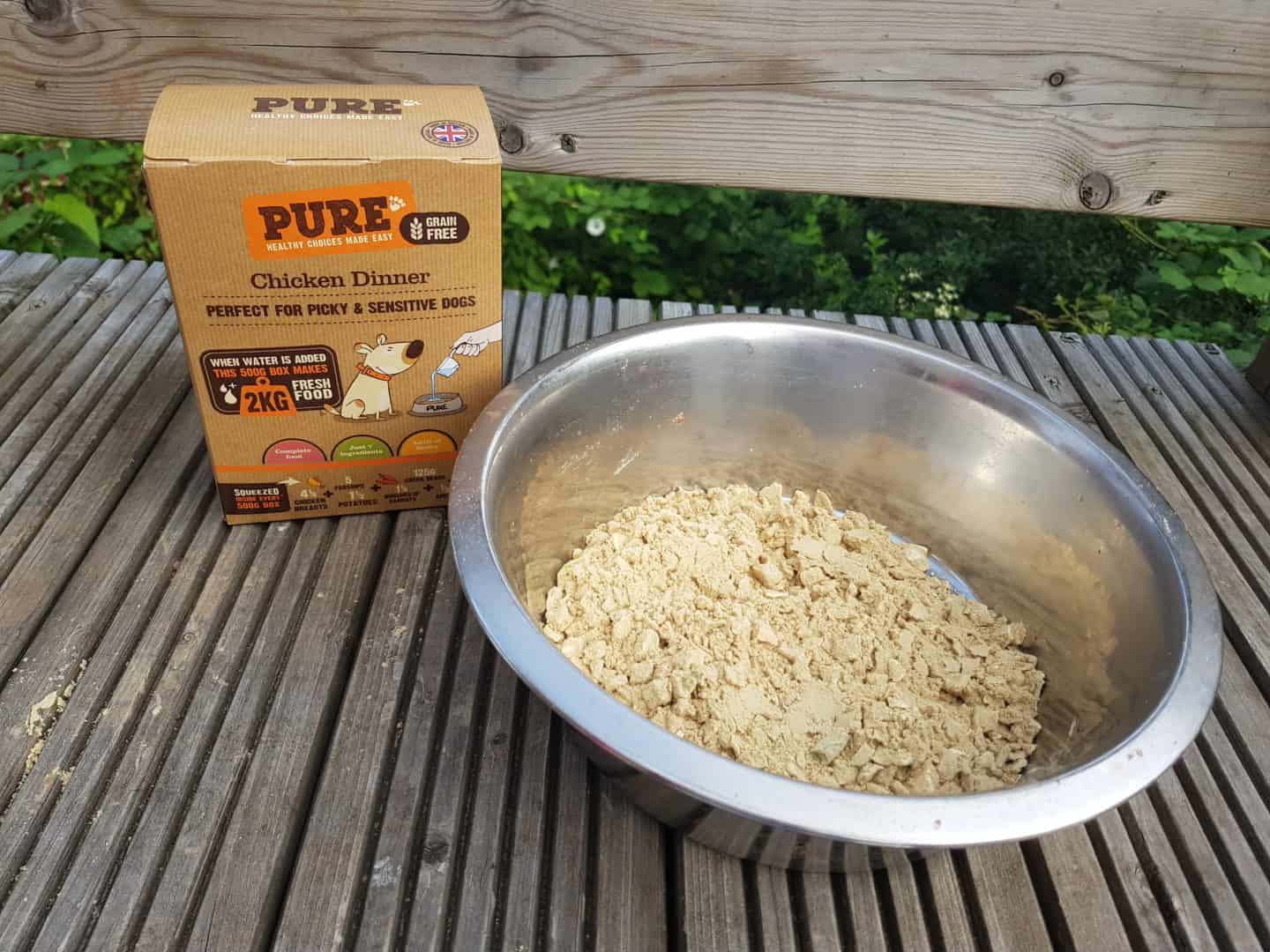Dehydrated Pure Pet Food in a white metal bowl next to a box of Pure Dog Food.