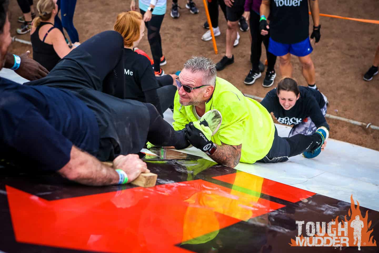 People helping each other up a high, sloping wall during a Tough Mudder event