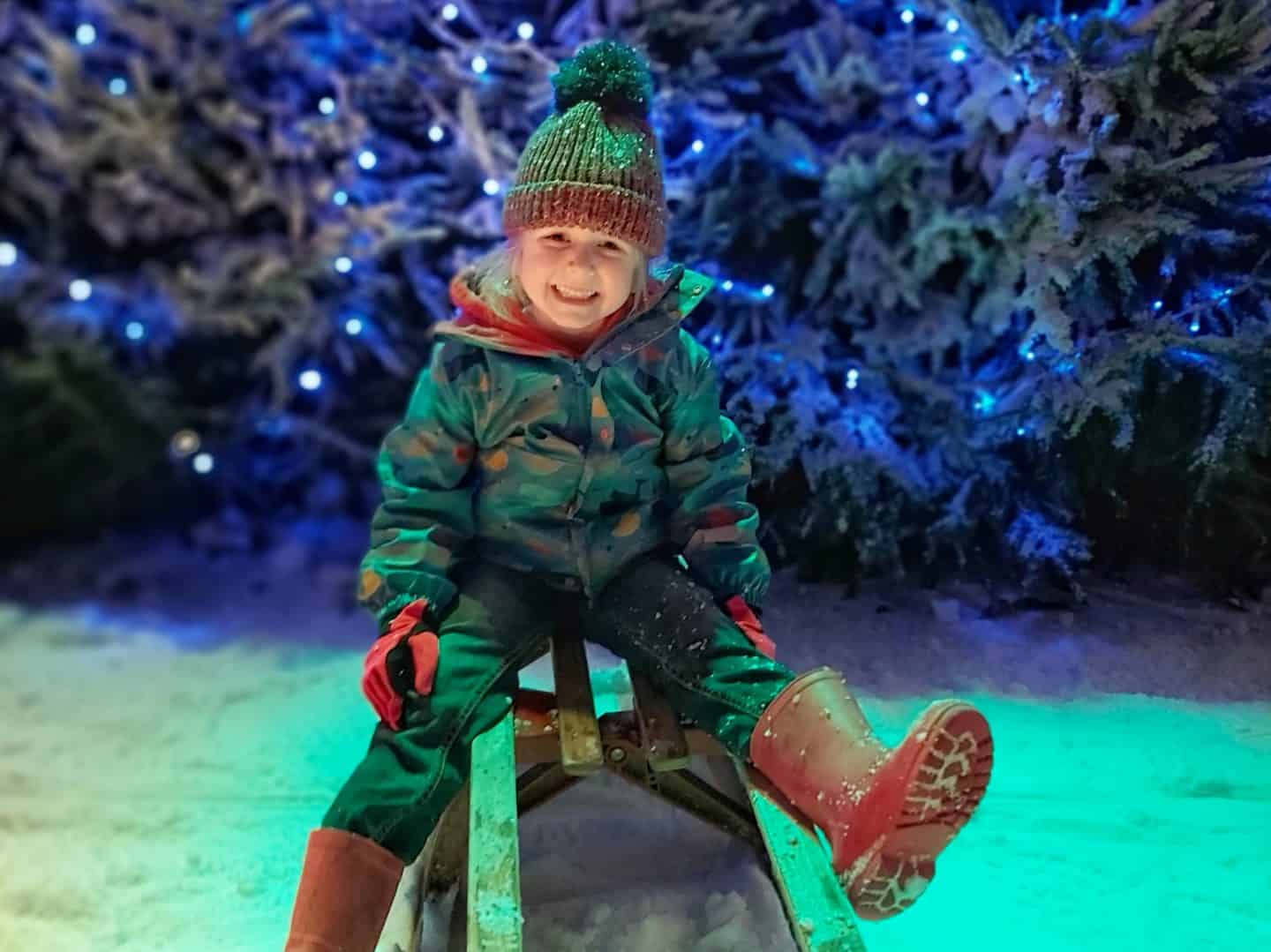 Girl on a sledge with Christmas trees behind at the Snowdome in Staffordshire