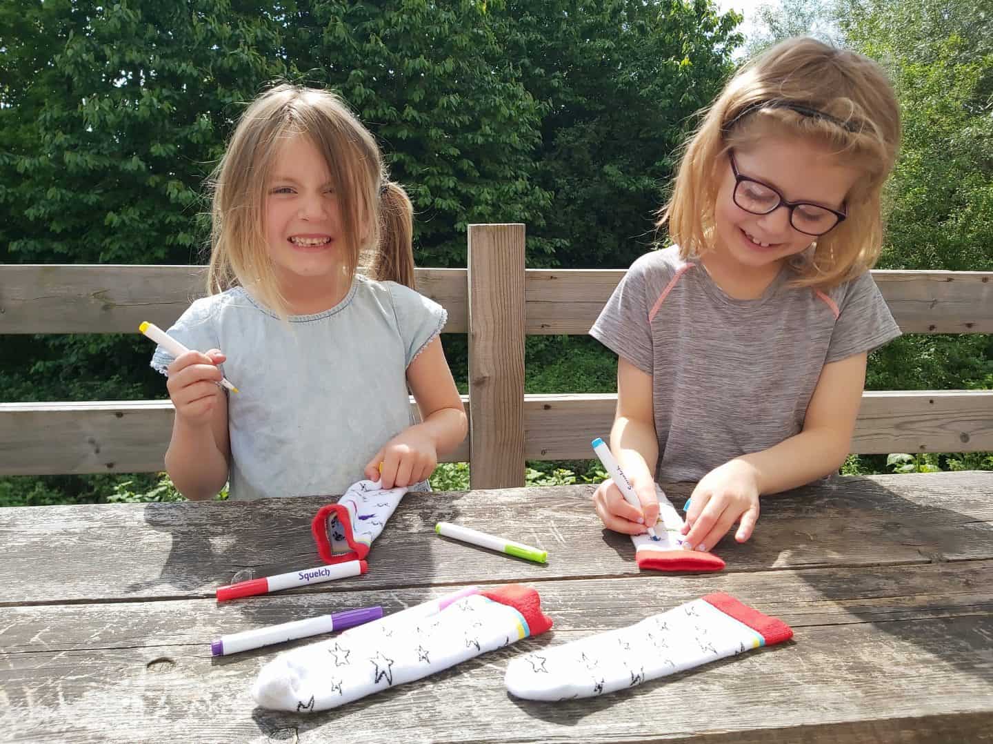Two little girls colouring in stars on white socks with red trim 