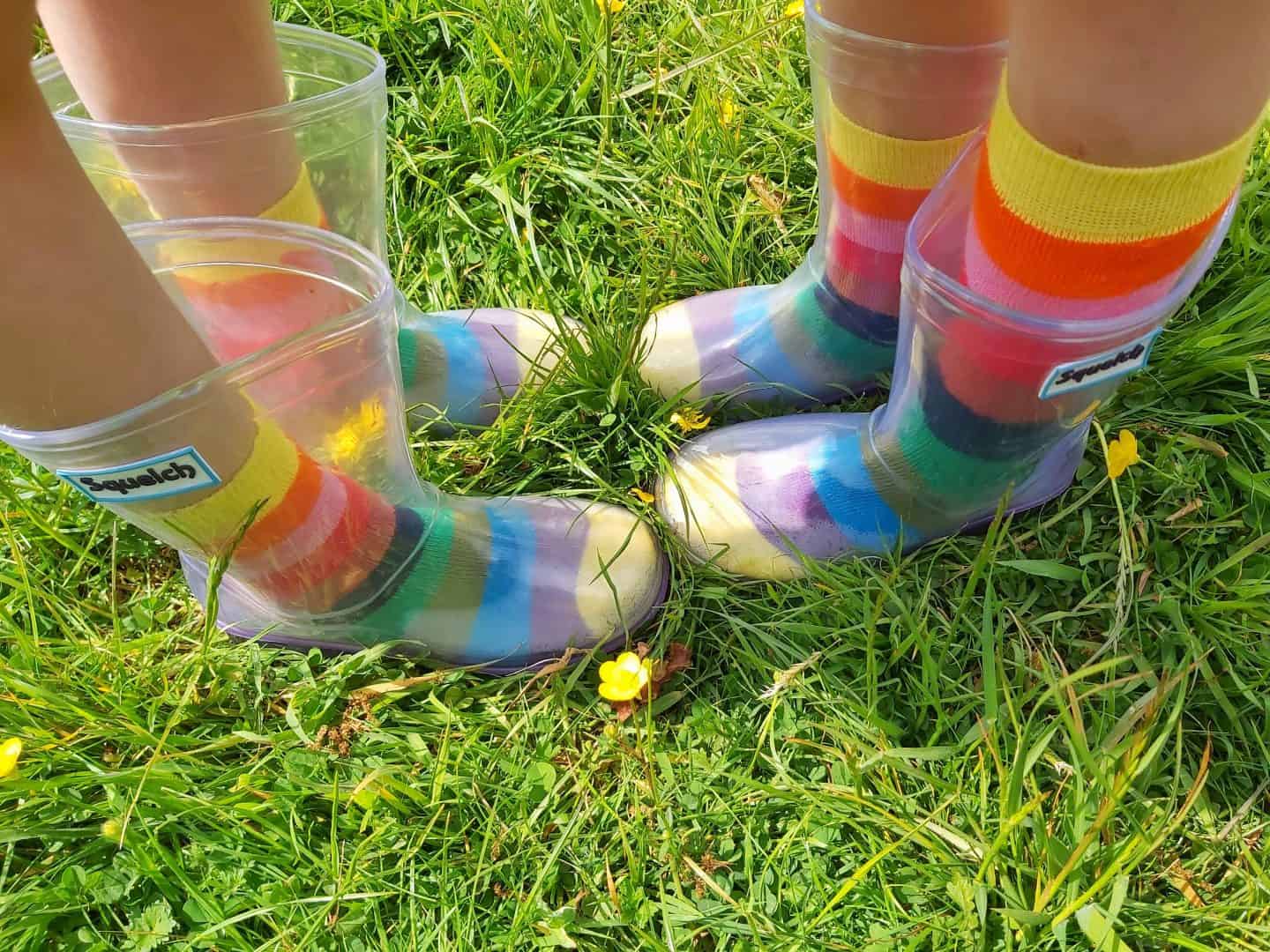 Two pairs of feet in see through wellies with rainbow socks
