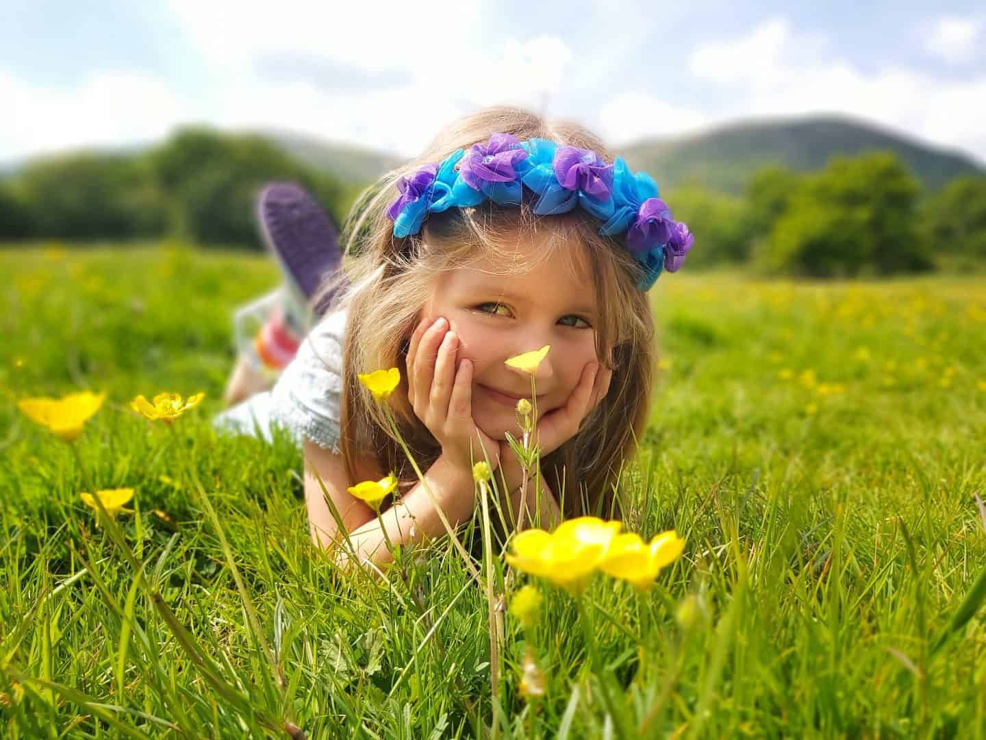 Little girl lying in a field with buttercups in foreground and hills behind