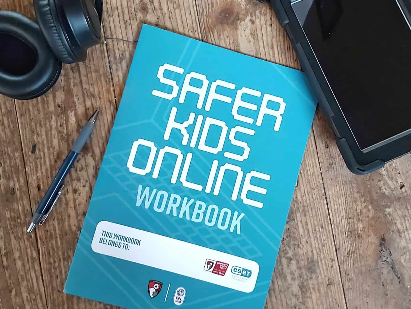 ESET Safer kids online workbook on wooden background with tablet, headphones and phone beside