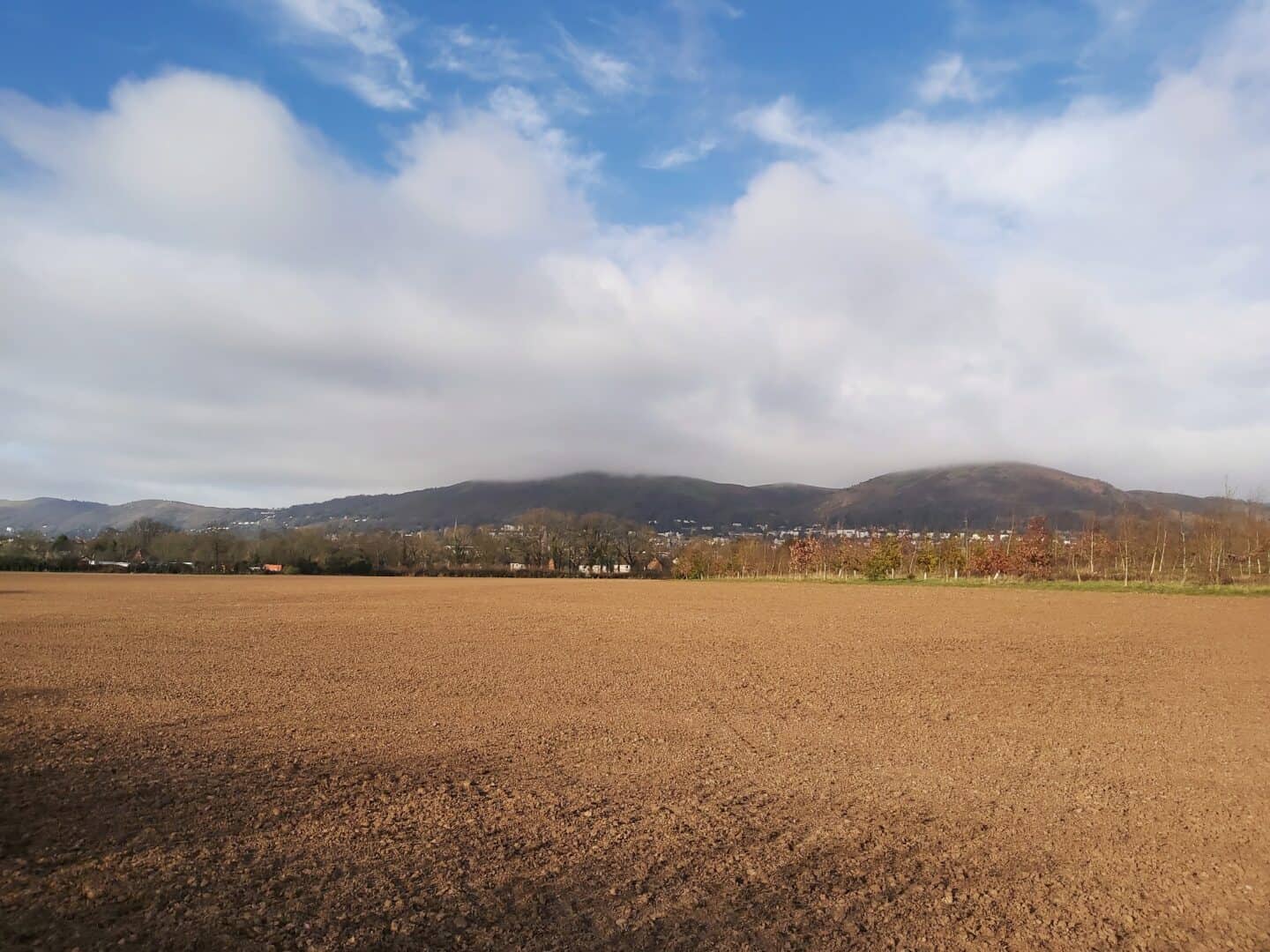 Ploughed field with Malvern Hills in the background. The tops of the hills are in cloud. 