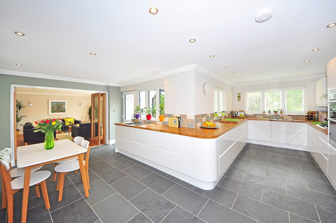Large kitchen with white units and grey floor and dining table 