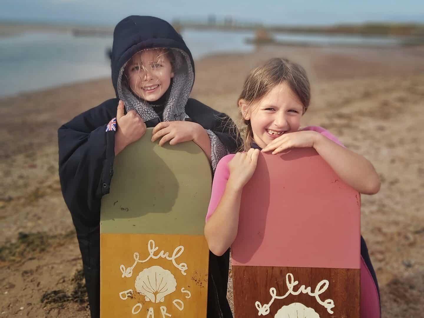 Two girls standing on a beach holding wooden betula handmade bodyboards