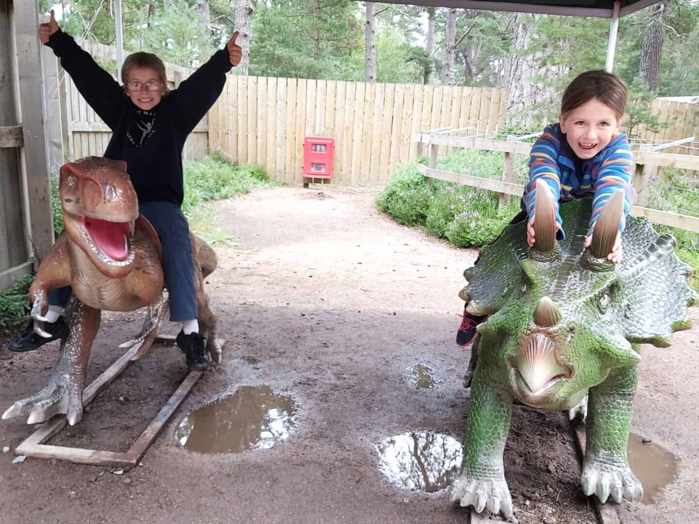 Family road trip itinerary: From the West Midlands to the Scottish Highlands. Photo of two girls on model dinosaurs at Landmark theme park near Aviemore.  