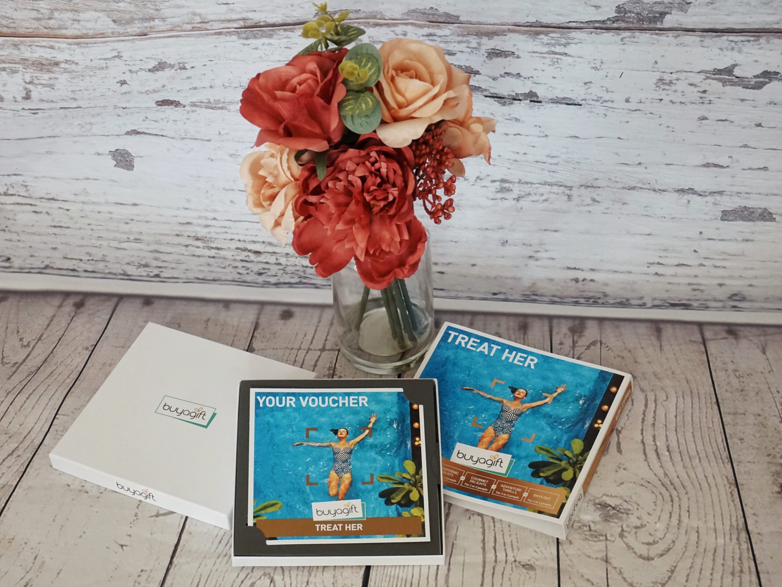 Treat her buy a gift voucher presented on a wooden background with a vase of red and peach flowers behind. Vouchers make great Ethical Mother's Day Gifts allowing mums to choose their own experience.  