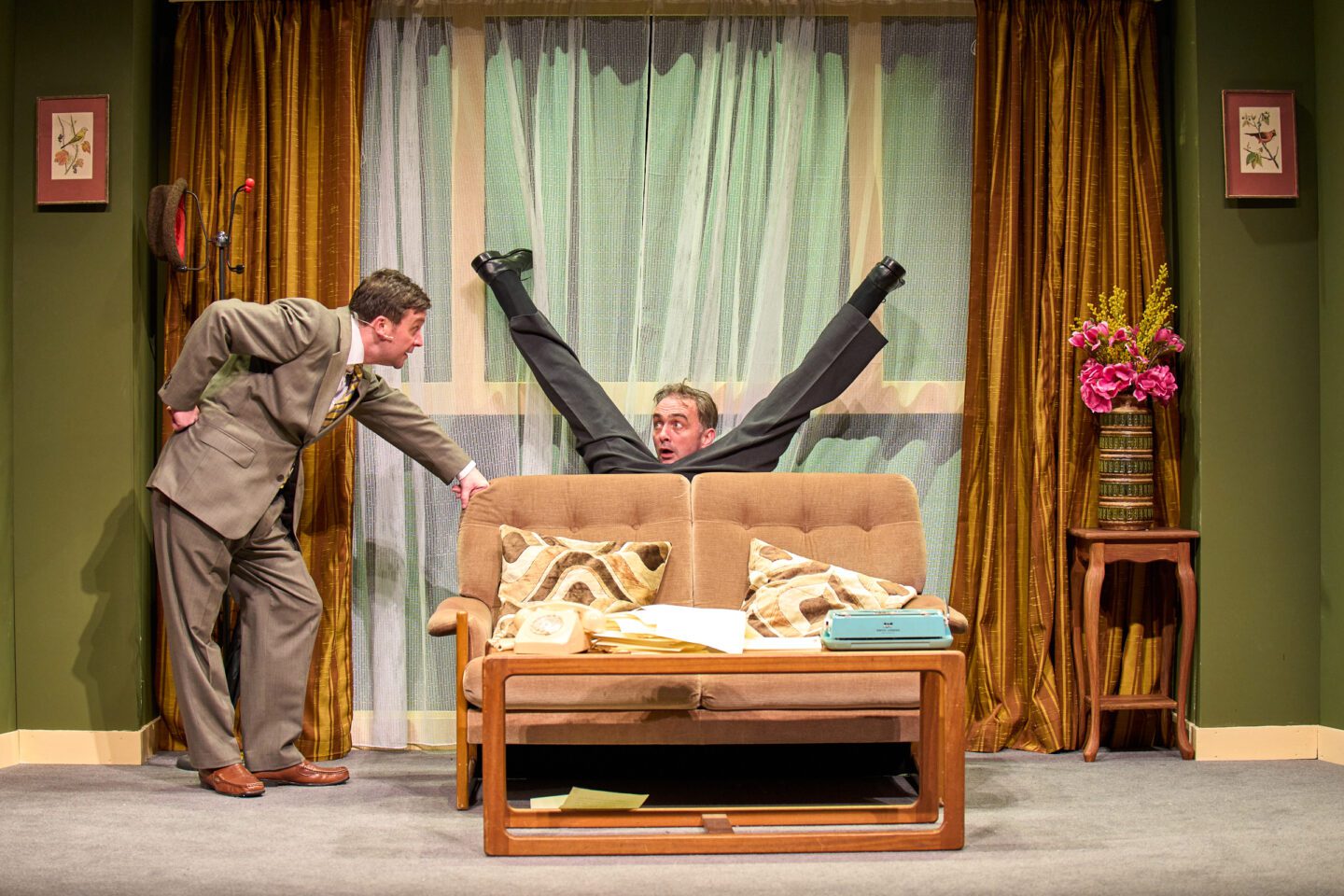 The Play What I Wrote at Malvern Theatres featuring Dennis Herdman falling behind a sofa and Thom Tuck watching on