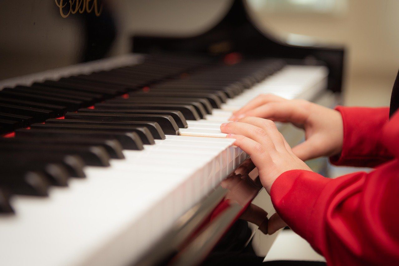 Child's hands playing the piano. Child wearing jumper with red sleeves. 