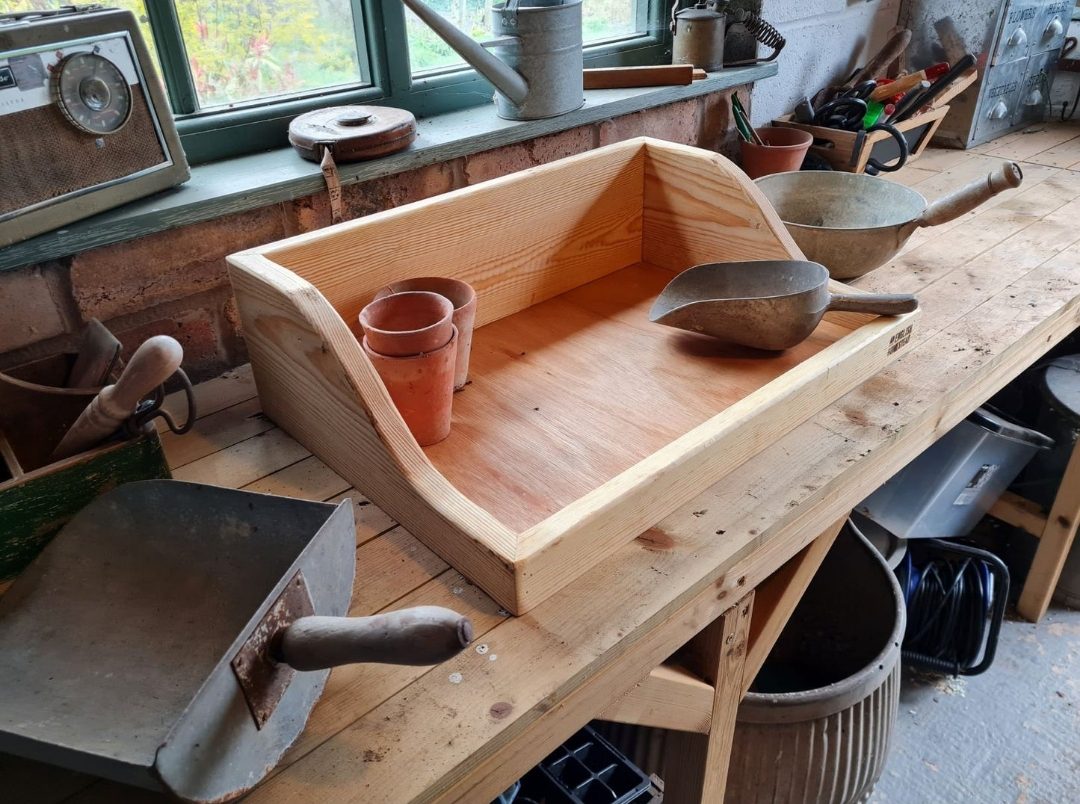Handmade wooden potting trays make ideal ethical mother's day gifts. Pictured in a workshop with pots and a trowel in the tray.  