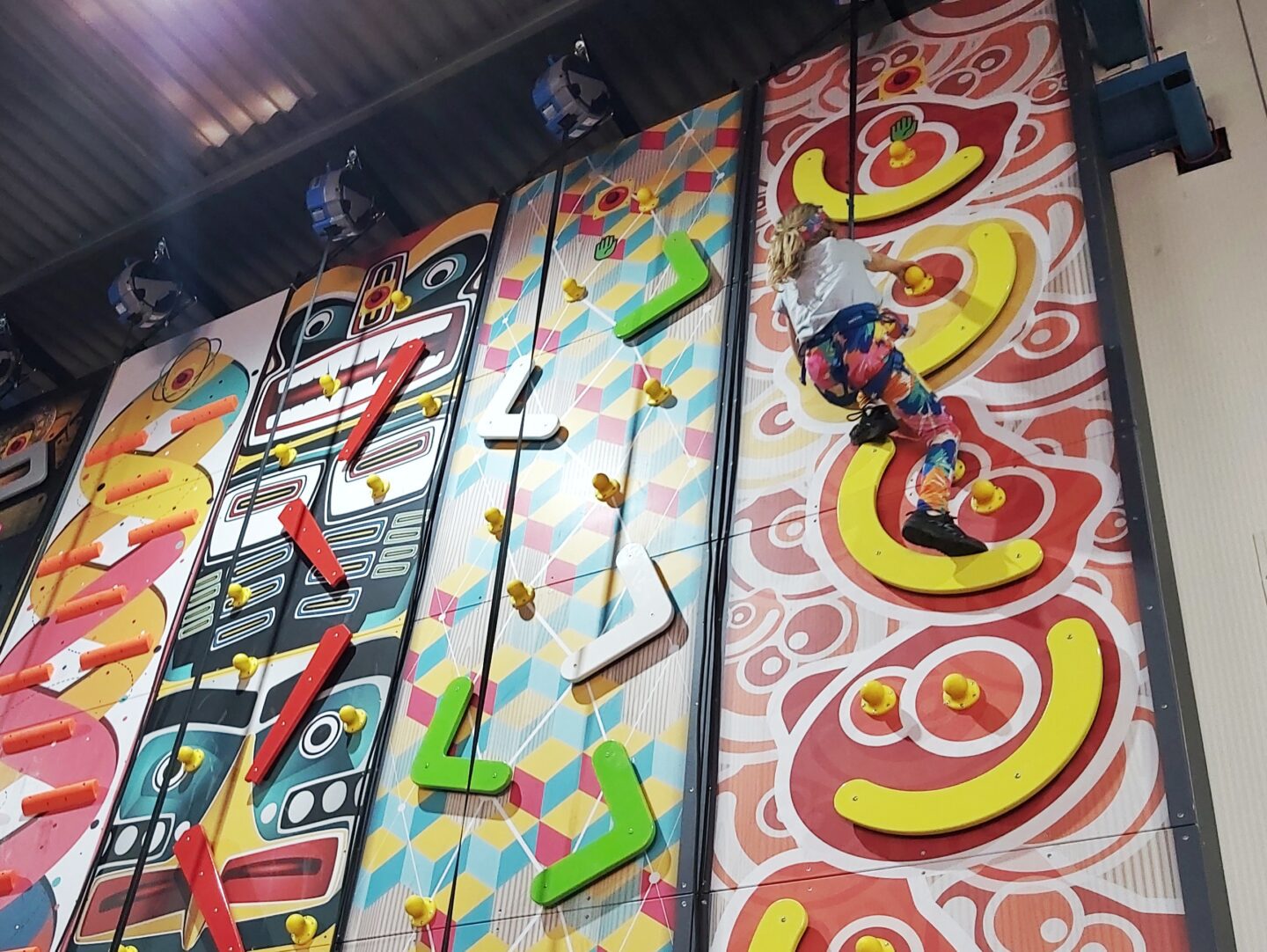 Indoor climbing wall with girl at top of wall on right hand side 