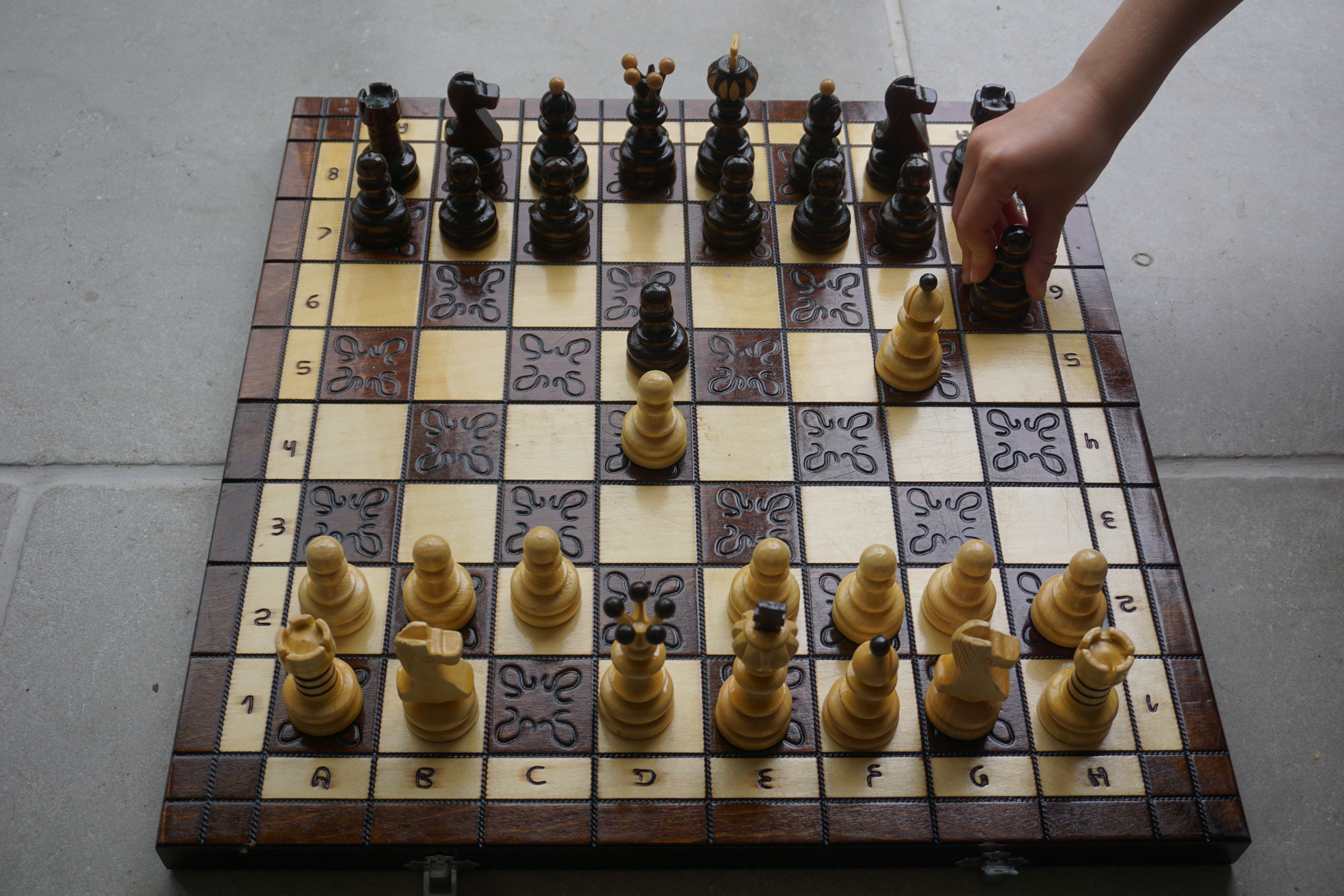 Chess is a time old classic that will always be one of the best board games for tweens. Board depicted mid game with hand moving black pawn.