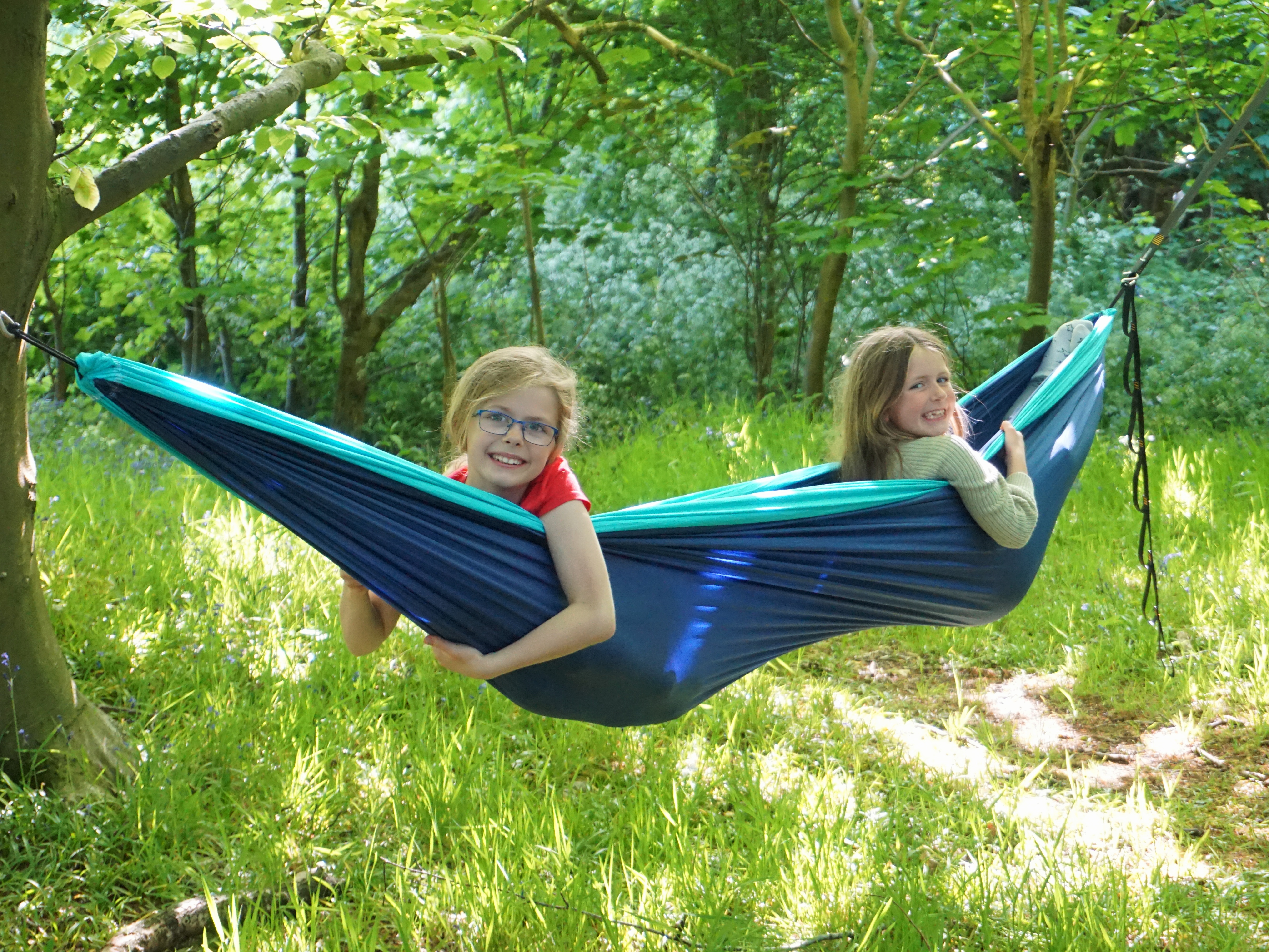 Two girls in a blue hammock hanging from trees in a wood