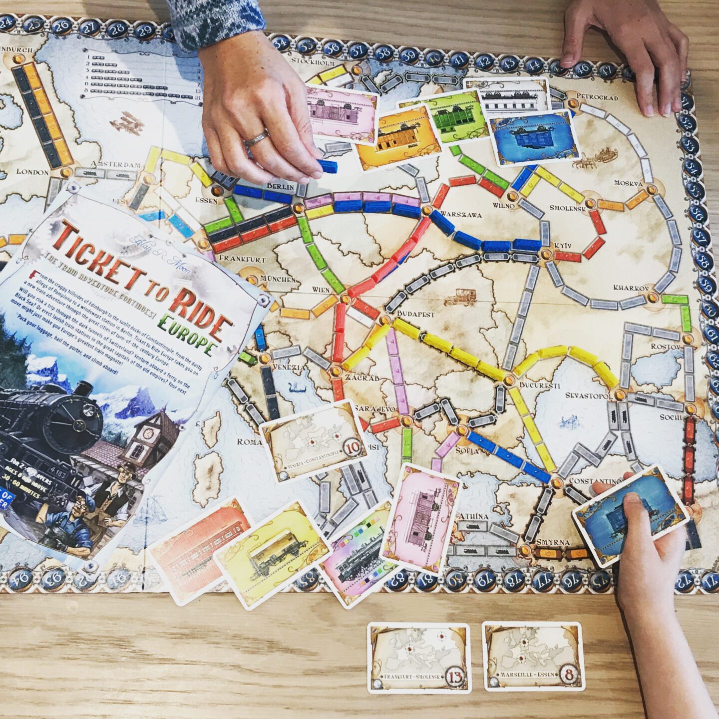 Ticket to ride board game shot from above showing two hands playing the game which is recommended as one of the best board games for tweens
