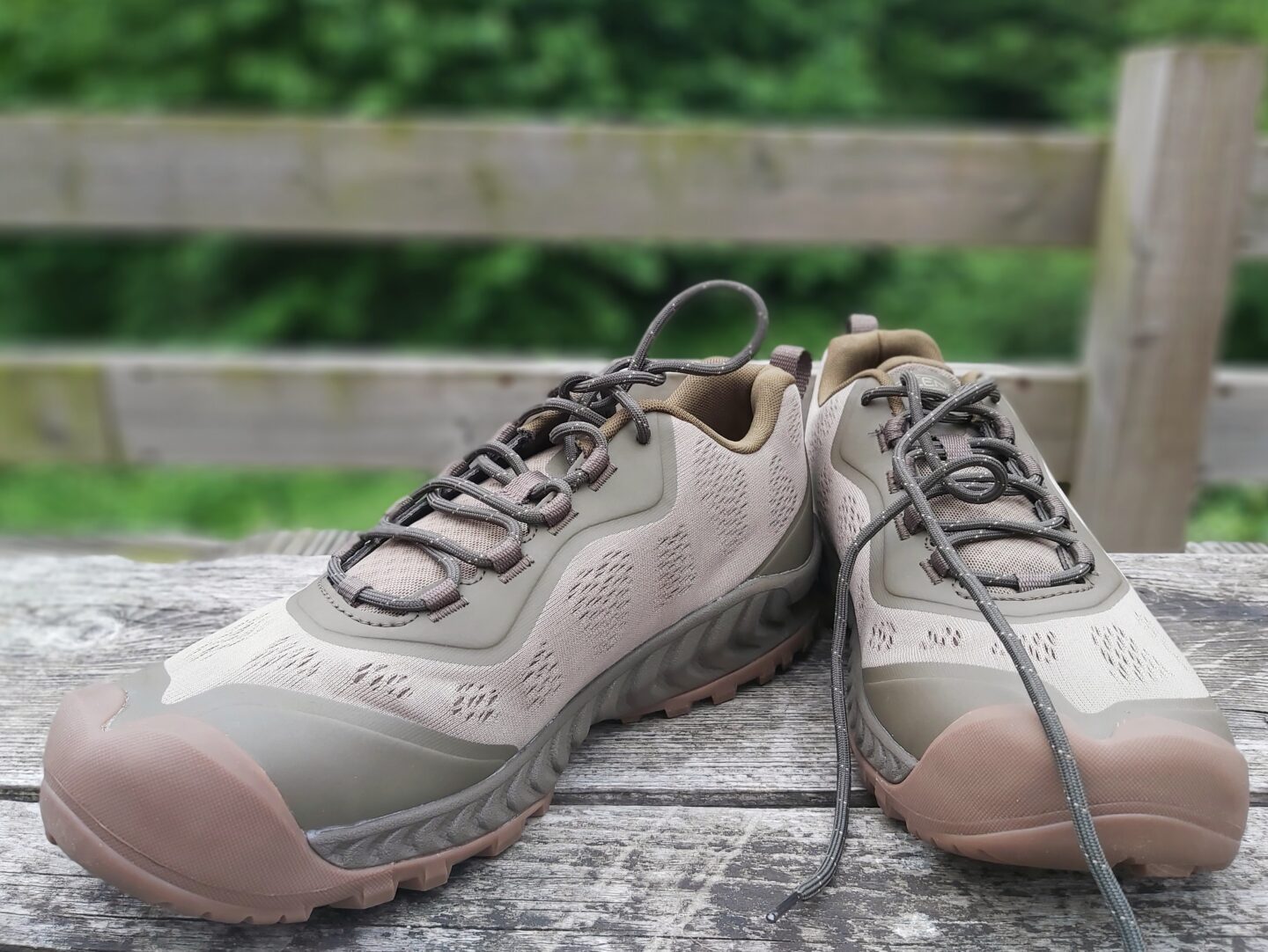 hiking trainers that would make ideal gifts for hikers displayed outside on a wooden backdrop with blurred green trees in background