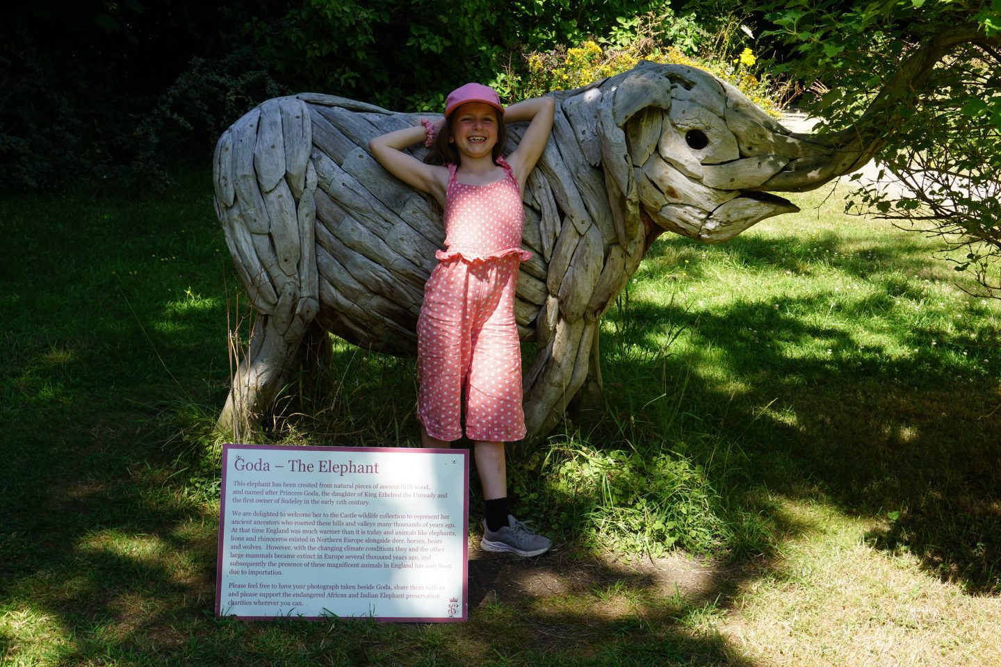 girl dressed in pink leans against baby elephant sculpture at Sudeley Castle