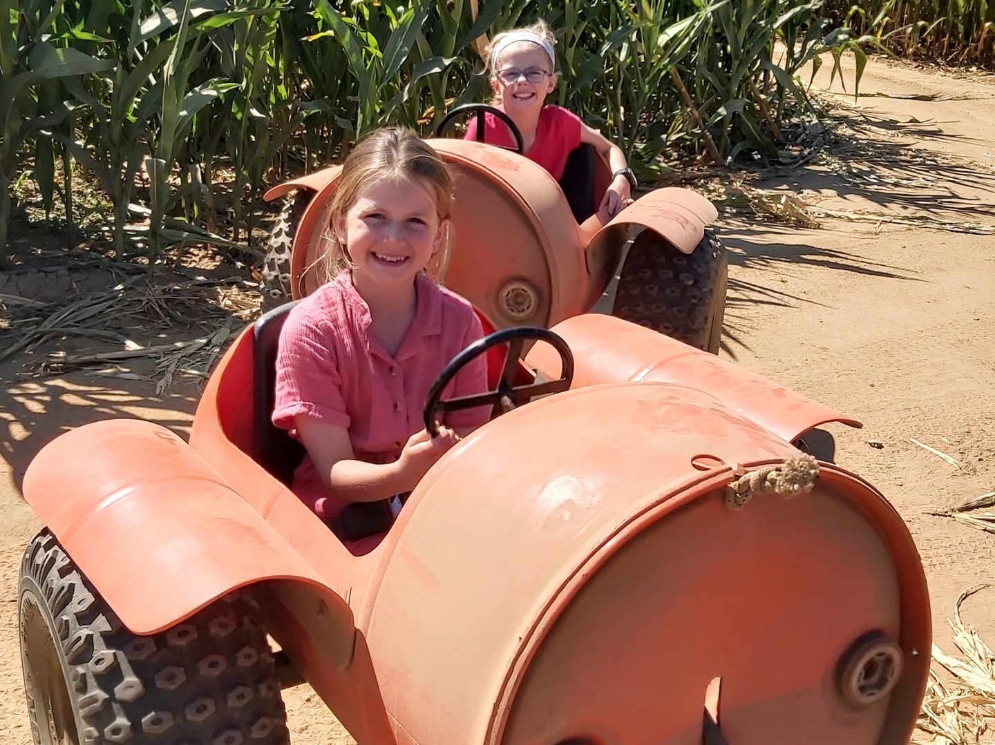 Two girls on barrel ride being pulled behind a tractor at Hirsty's Family Fun Park with maize behind