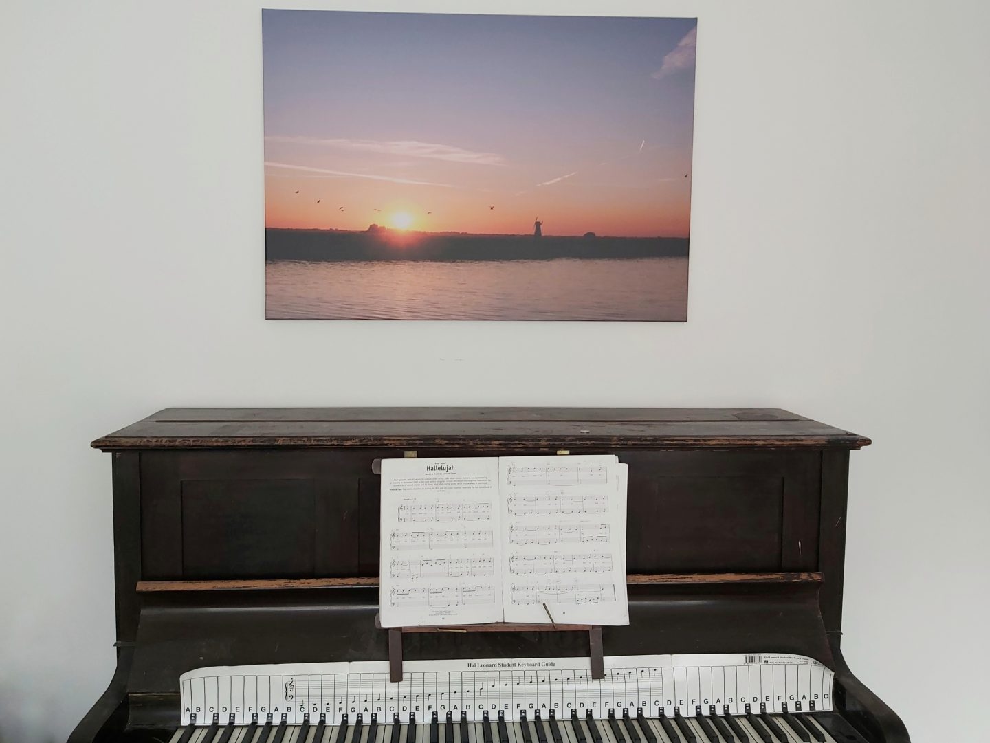 Canvas image of a sunset hanging above a piano against a white wall