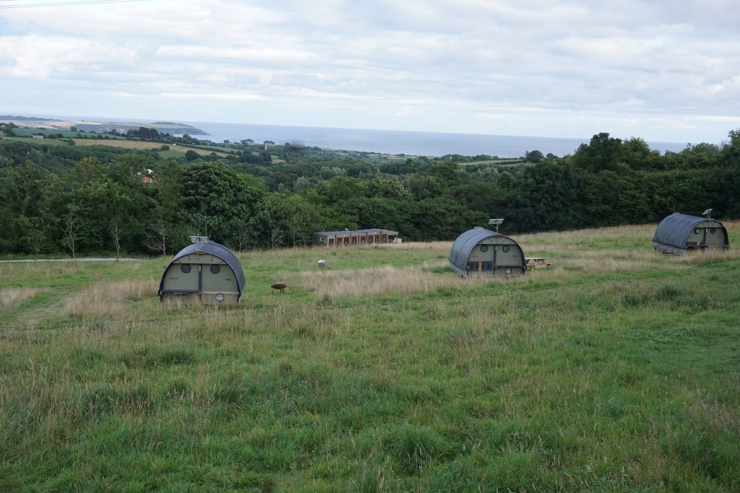 View of Landpods at the YHA Eden Project campsite on grass with hedge and sea in background 
