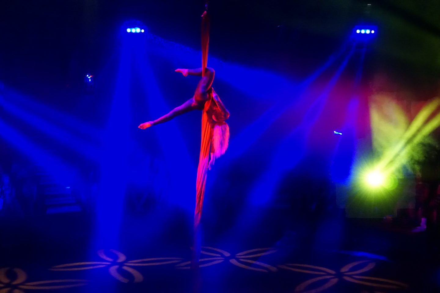 Acrobat in the Great Yarmouth hippodrome circus hanging from the ceiling wearing pink with blue lights around