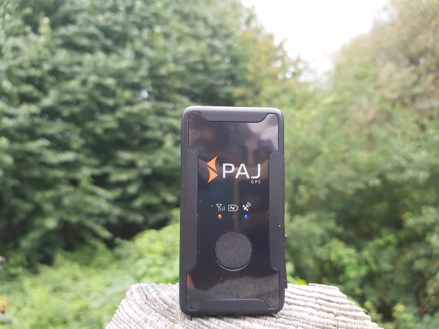 PAJ Easy Finder GPS Tracker displayed on top of a wooden post with trees in the background