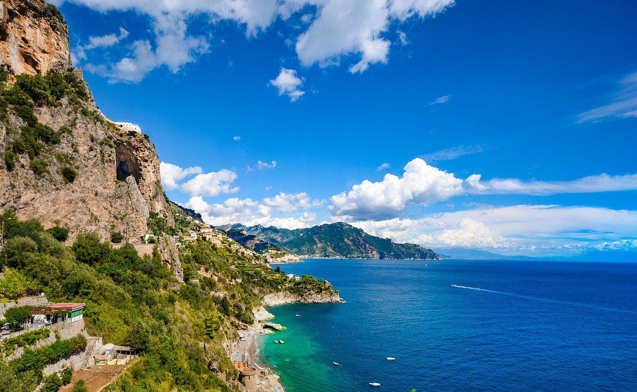 Blue sea on Amalfi Coast with cliff to left hand side and blue sky with few white clouds