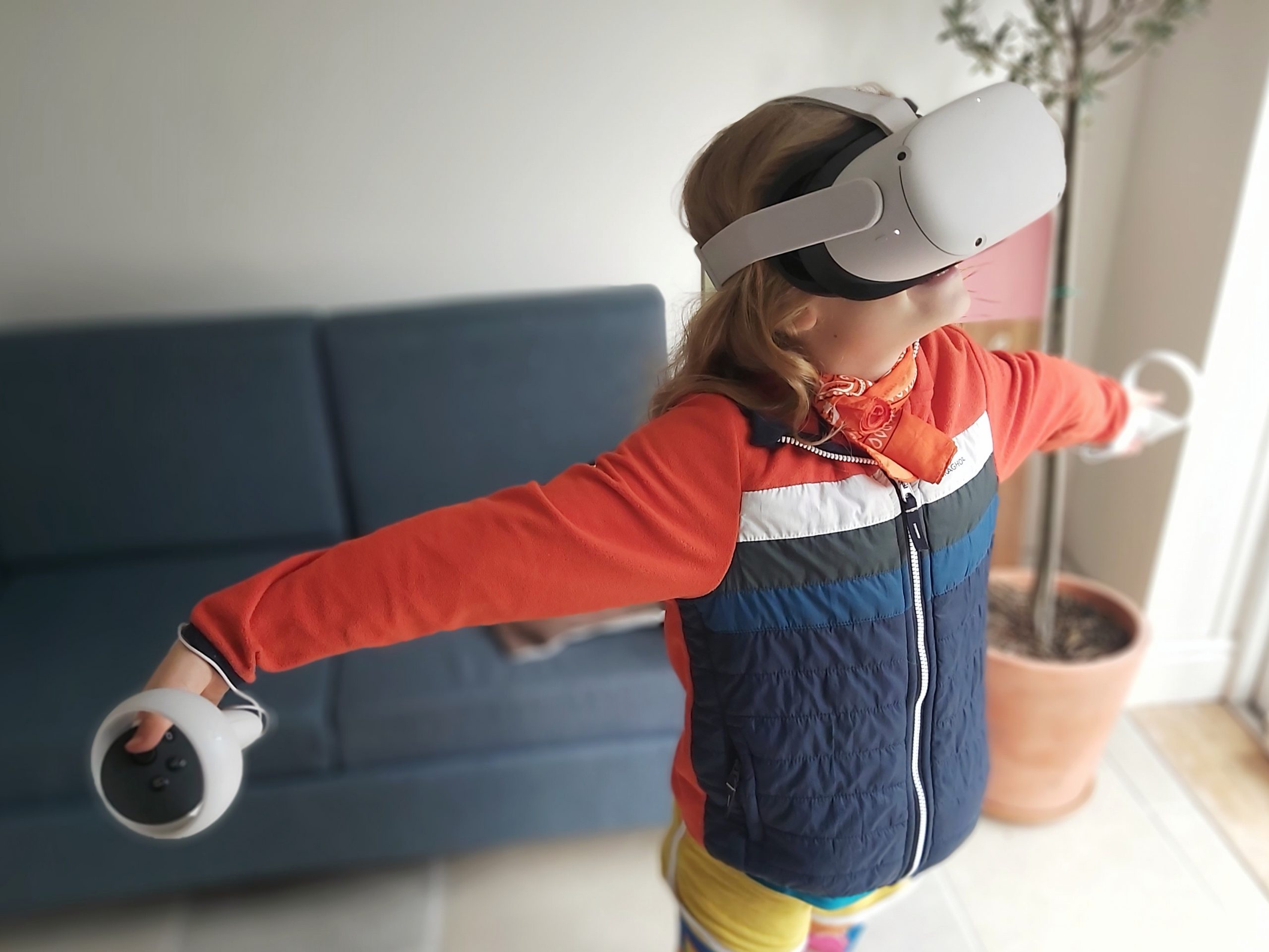 Girl in blue and orange jacket playing on the Oculus Meta Quest 2 VR Headset with arms outstretched
