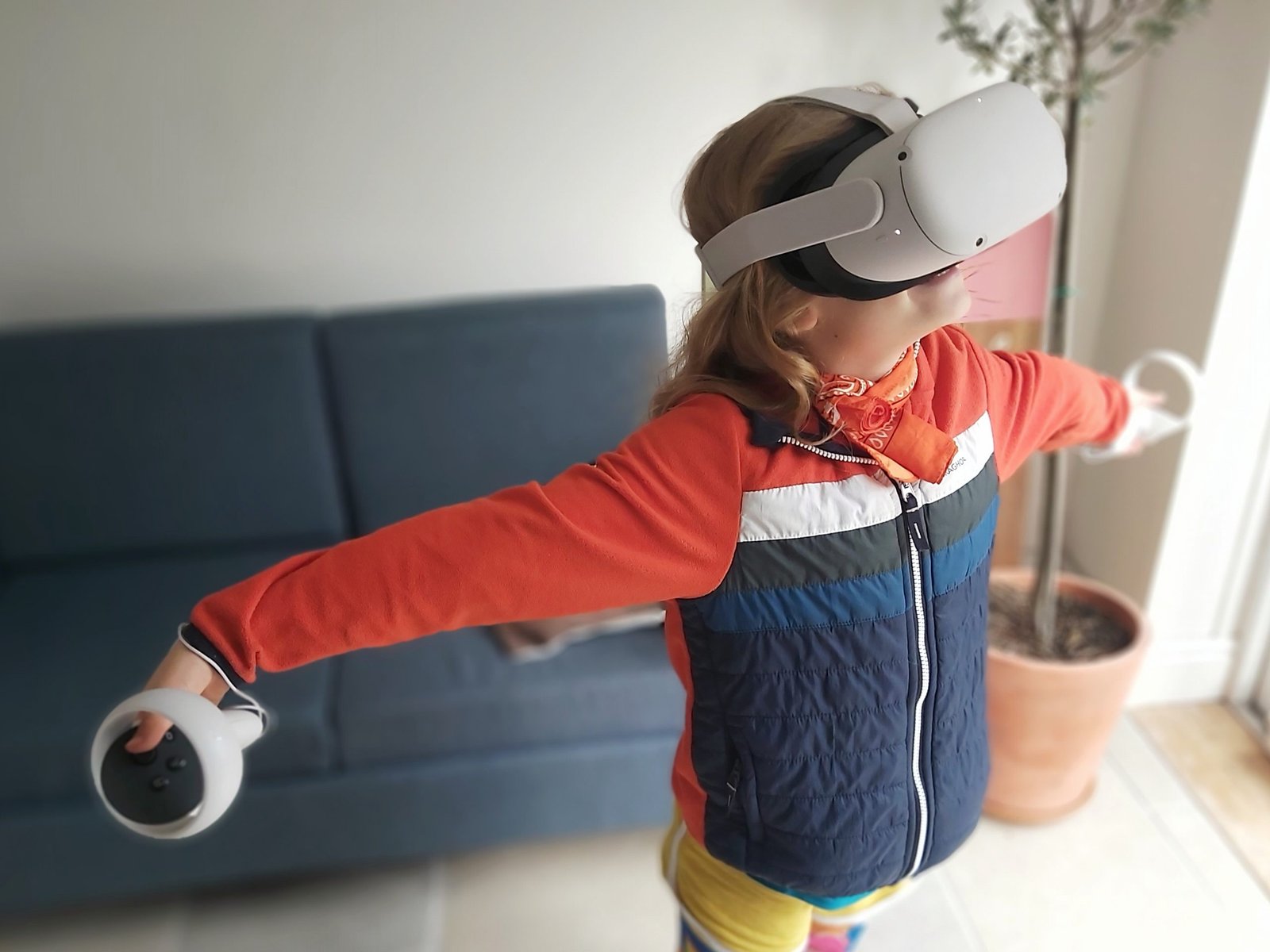 Girl in blue and orange jacket playing on the Oculus Meta Quest 2 VR Headset with arms outstretched