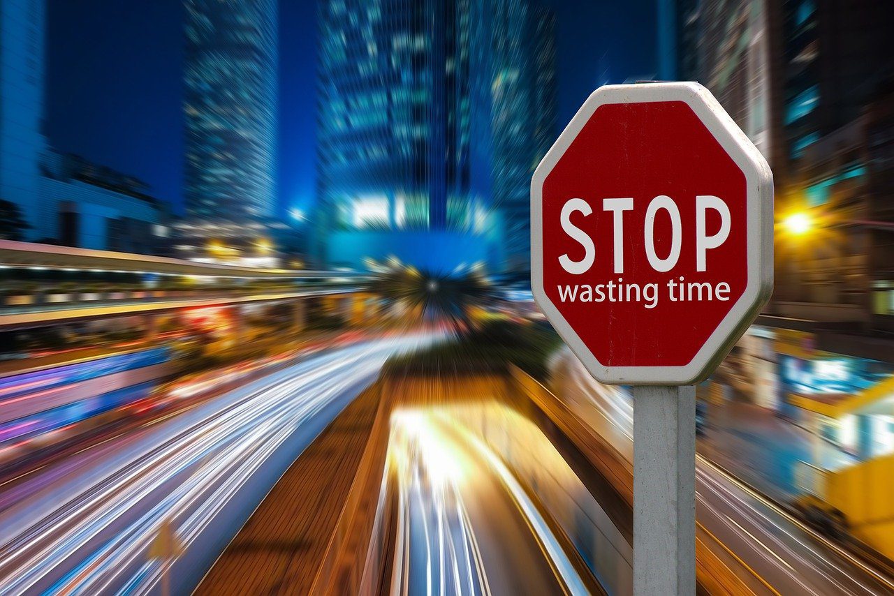 Traffic stop sign with "wasting time" written underneath stop. Road with moving lights and skyscrapers in the background. 