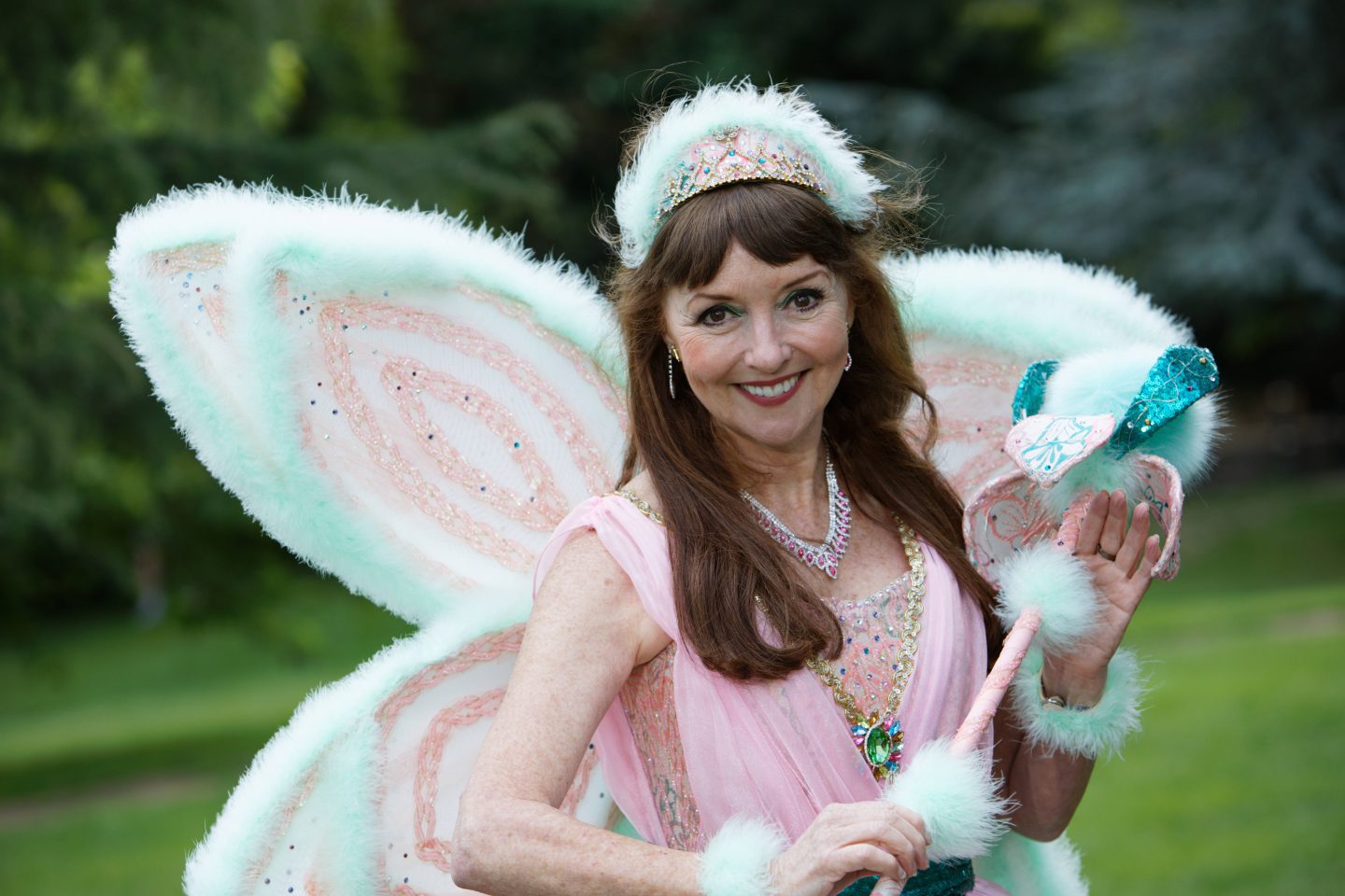 Melanie Walters as Fairy Bon Bon in Malvern Theatres Pantomime 2022 Beauty and the Beast taken outdoors with green grass and trees behind