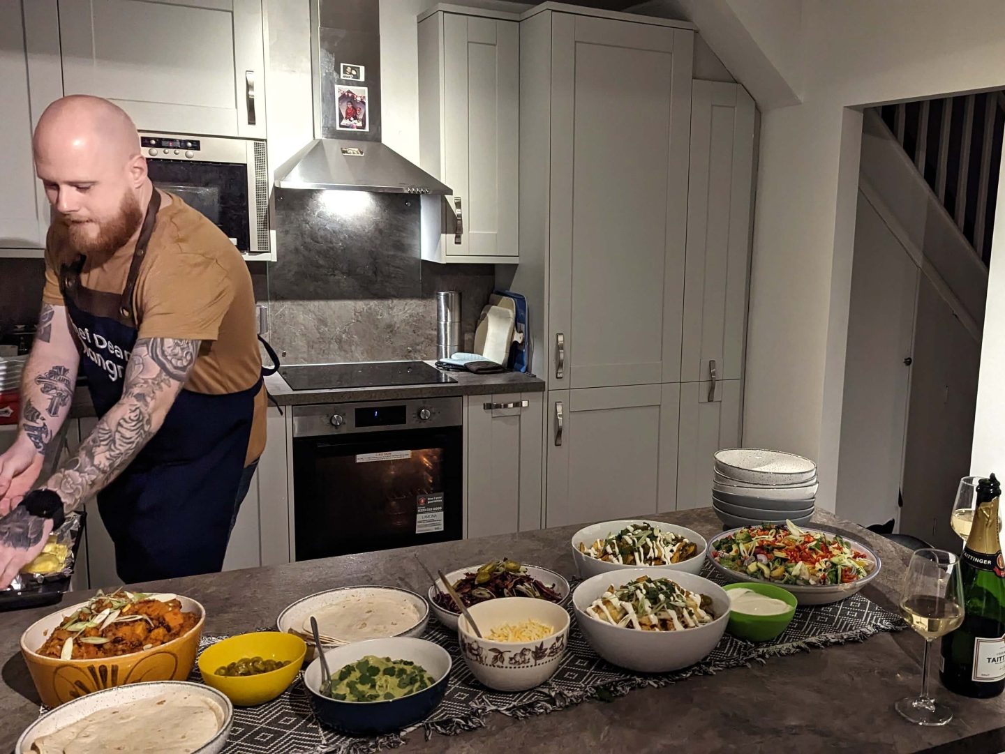 Bowls of Mexican food prepared by yhangry chef Dean on a dark grey table in a light grey kitchen with Dean on left hand side of shot and oven with chrome extractor behind him 