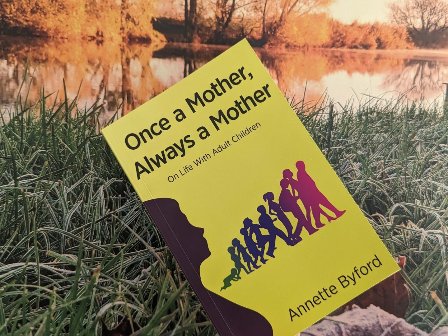 Once a Mother Always a Mother yellow book by Annette Byford displayed beside a river on frosted grass