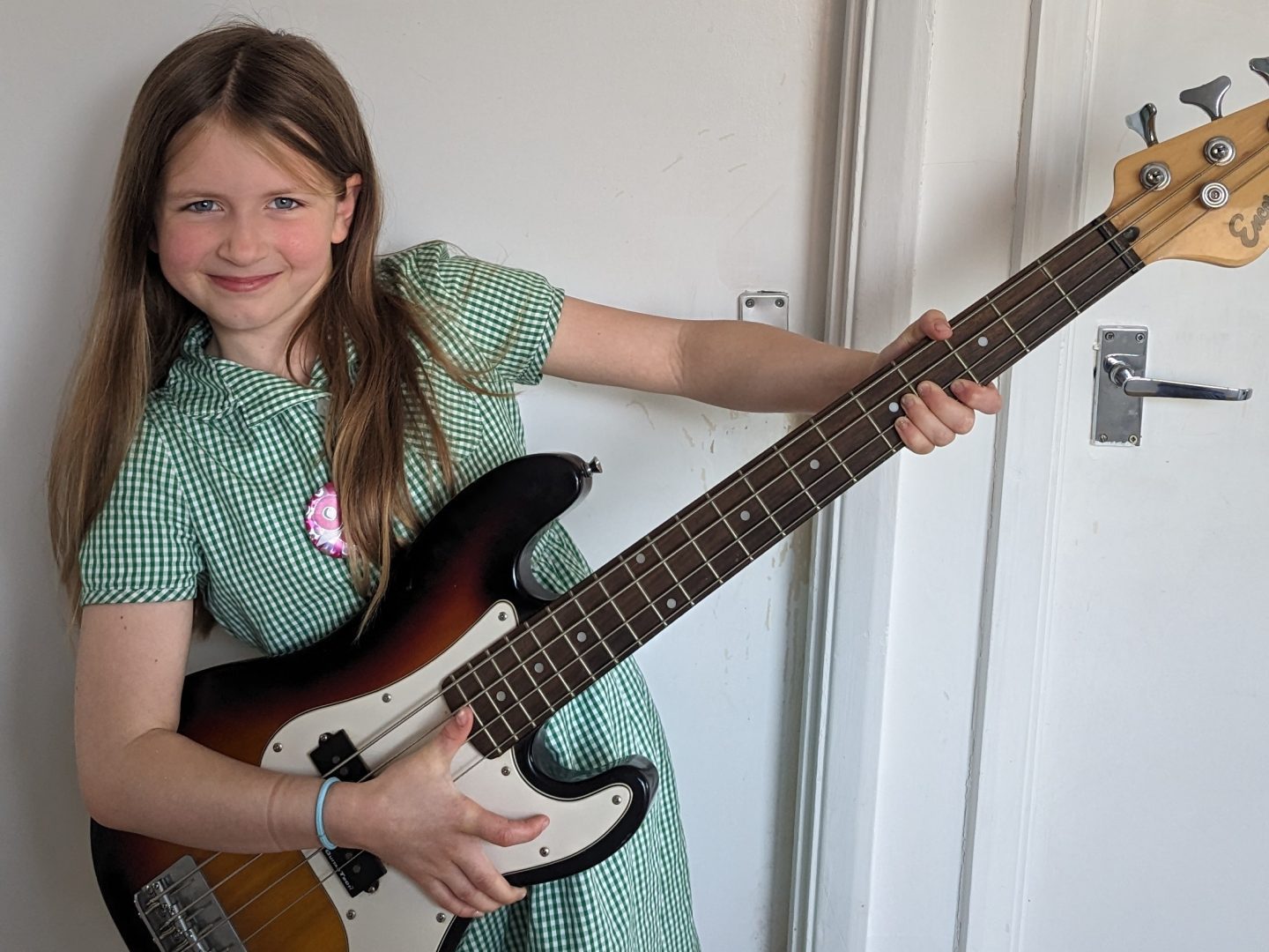 Lia in green and white summer school uniform dress holding an electric bass guitar