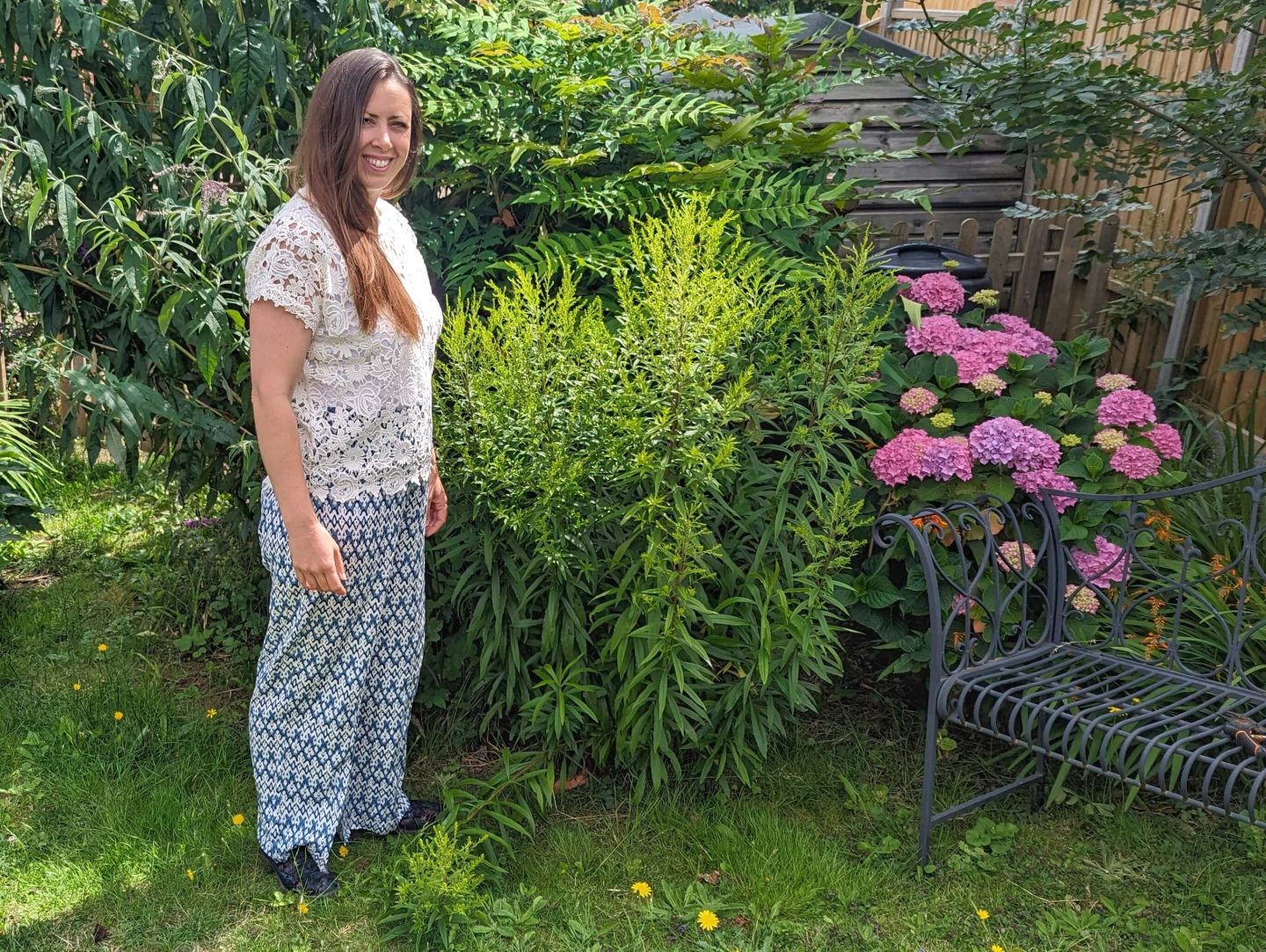 Natalie standing in the garden wearing Cotton Traders Jasmine Harman Collection top in natural colour and patterned blue trousers from the same collection