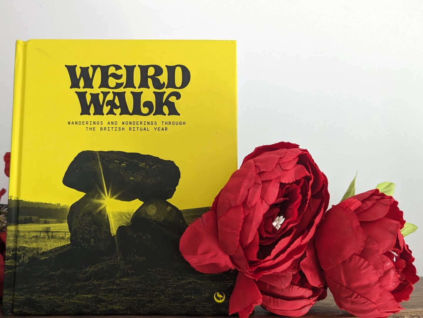 Yellow Weird Walk book with red flowers in front displayed on a wooden shelf