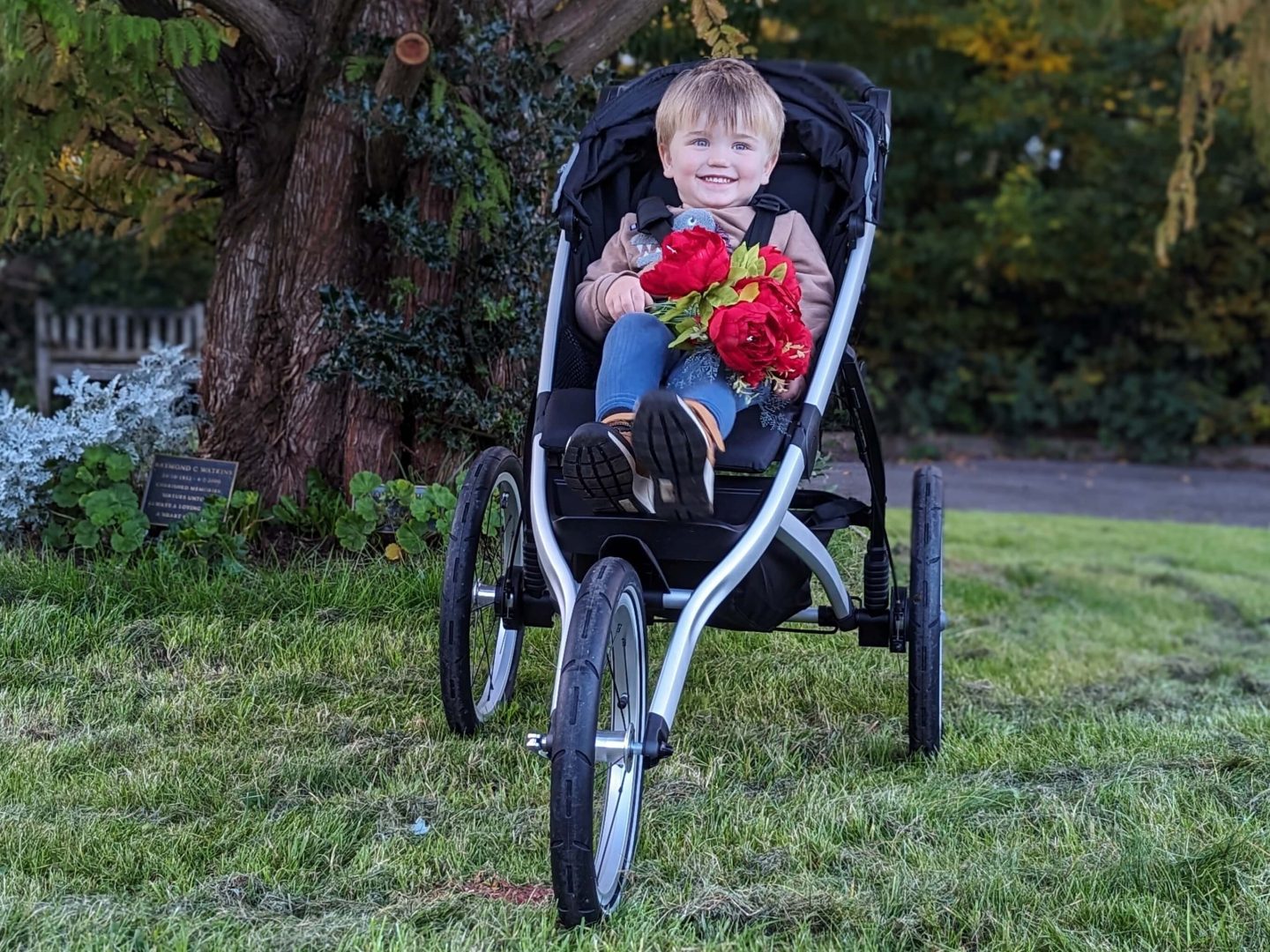 Little boy sitting in a Thule Glide 2 running buggy smiling and holding red flowers
