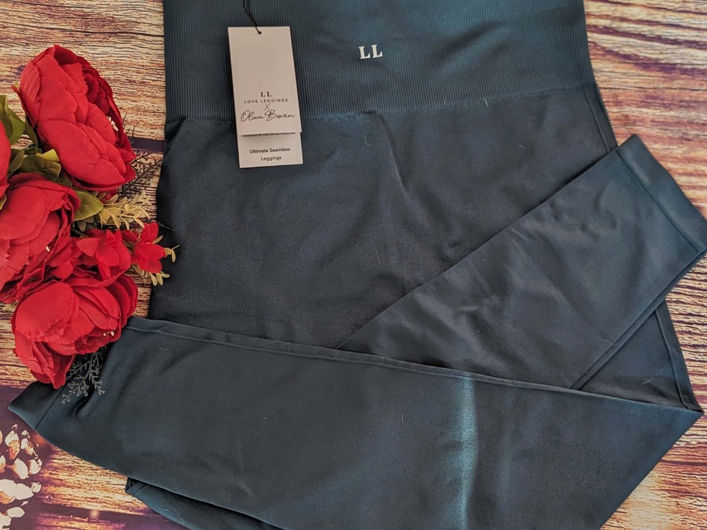 Aqua coloured high waisted leggings from Lovall displayed against a wooden backdrop with red flowers beside