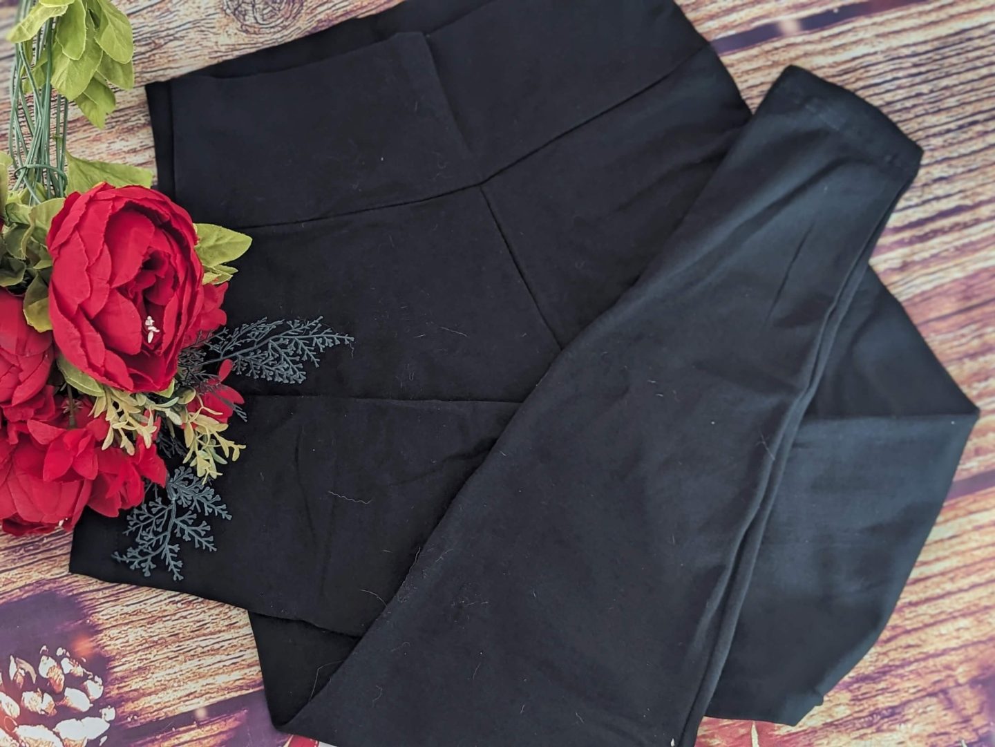 Black high waisted leggings from Lovall displayed against a wooden backdrop with red flowers beside