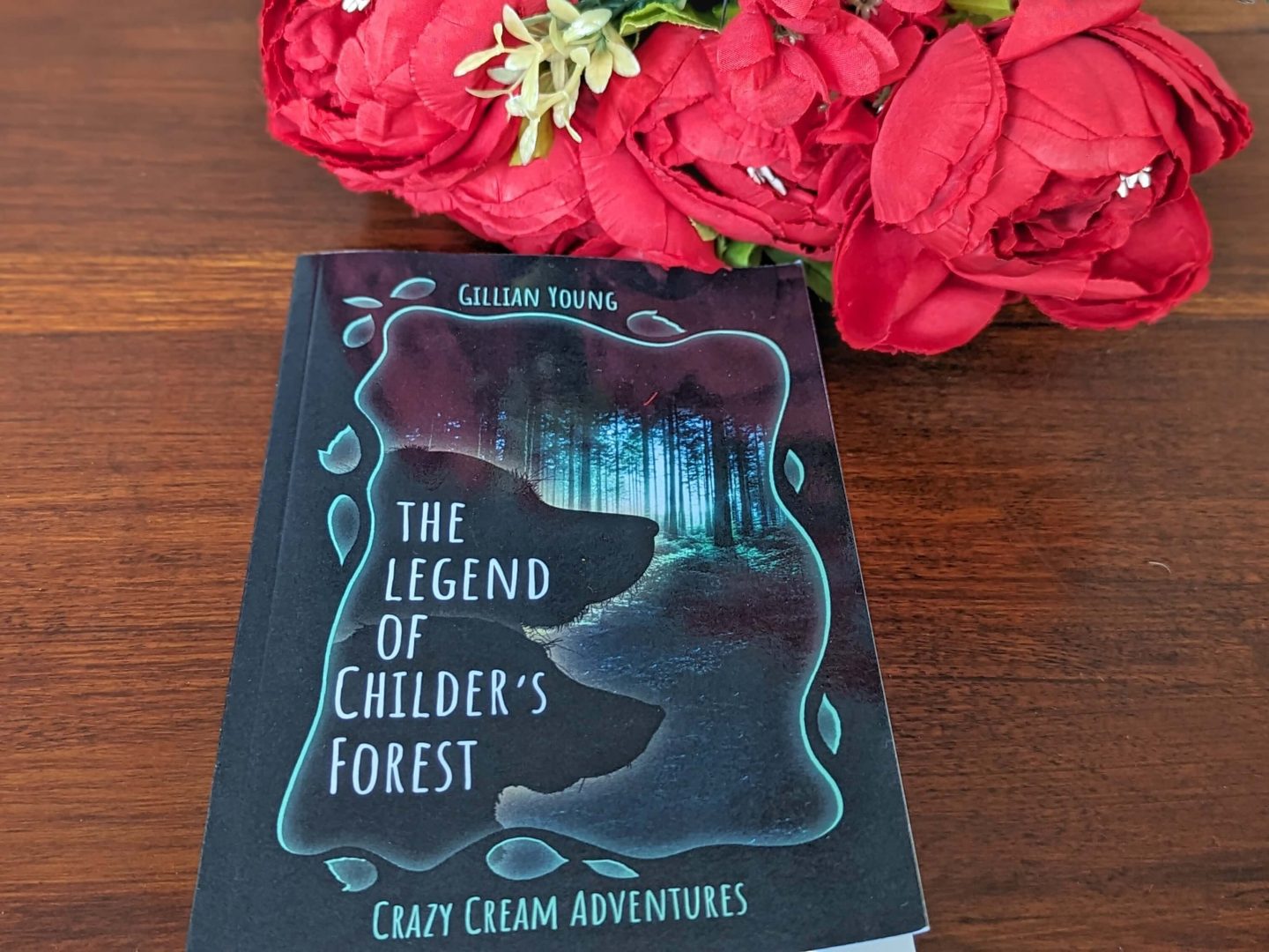 The Legend of Childer's Forest book displayed on a wooden table beside a bunch of red flowers for the something to read section of the four gift rule Christmas gift guide