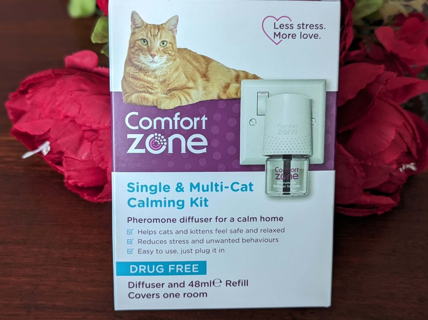 Comfort Zone Calming Diffuser for Cats displayed against a wooden background propped up by red flowers - something you need for cats in the four gift rule Christmas gift guide